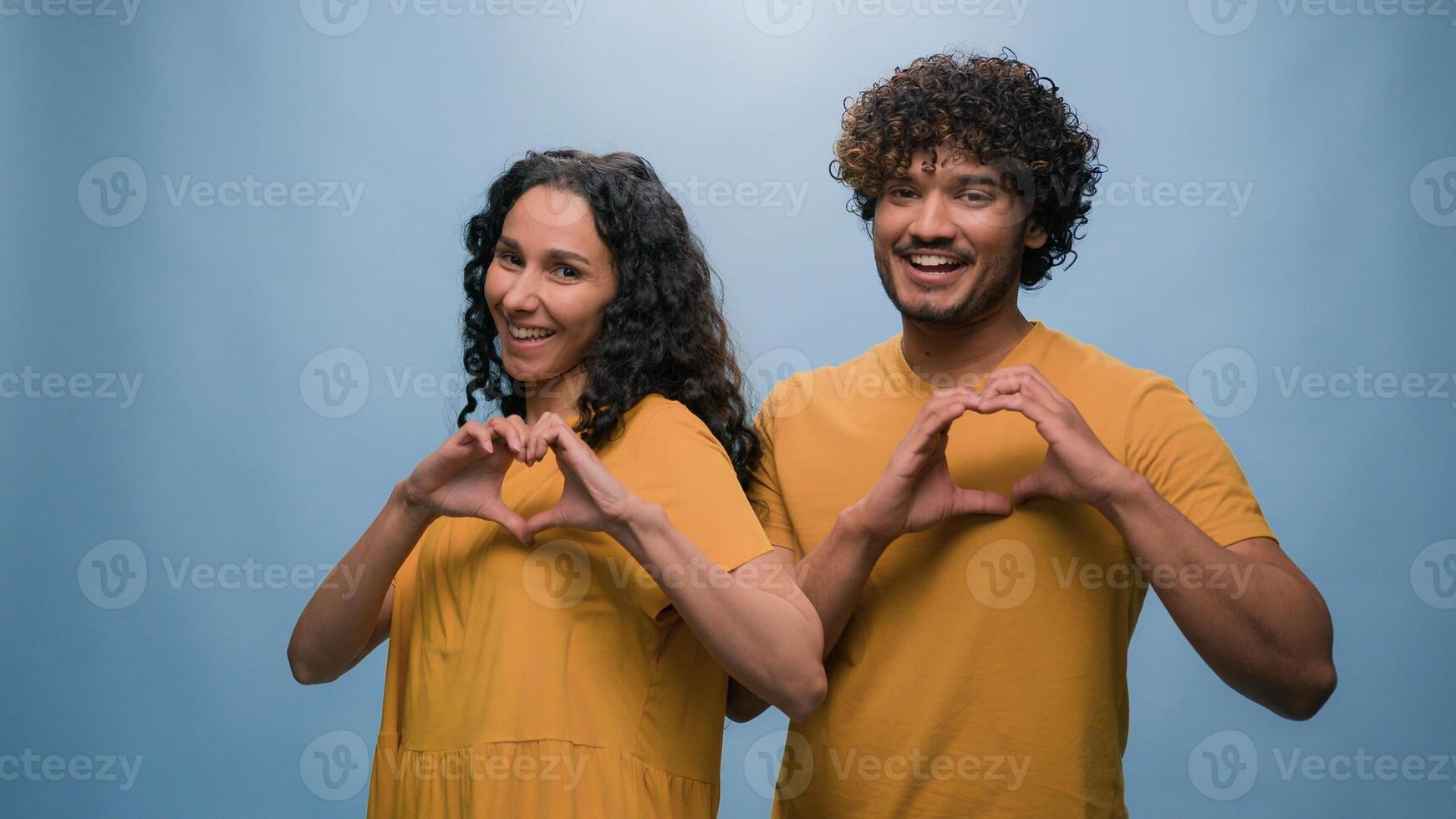 Studio portrait happy couple diverse multiracial man woman love joined fingers making heart shape St Valentines Day celebration romantic relationships married spouses sincere feelings blue background photo