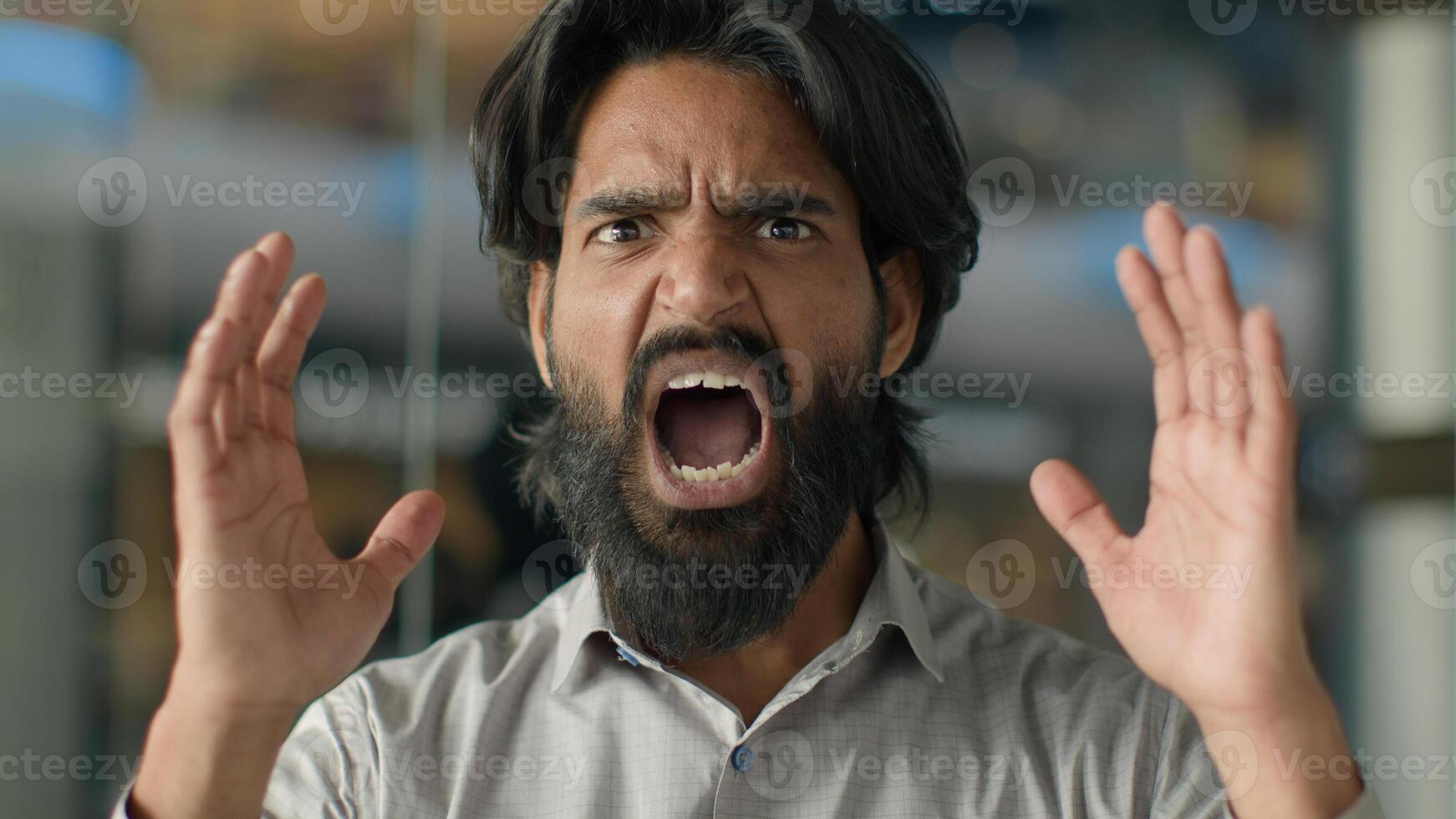 Close-up emotional angry aggressive furious displeased stressful irritated mad Indian bearded man guy shouting screaming yelling swearing shout scream looking at camera stressed male portrait indoors photo