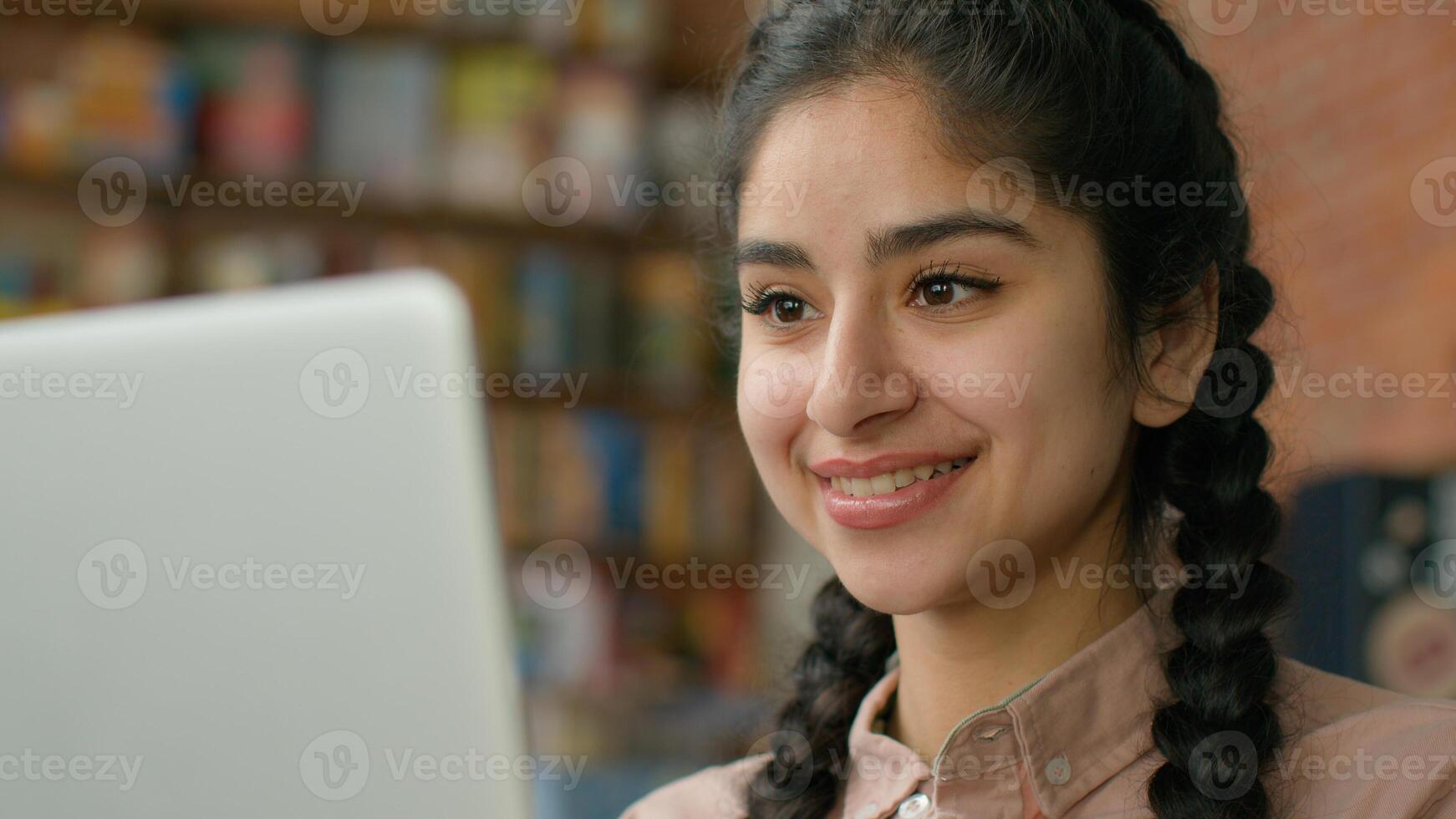 Close-up smiling young indian woman looking at laptop screen indoors checking email browsing social network hispanic girl student studying online remote chatting on internet typing message on computer photo