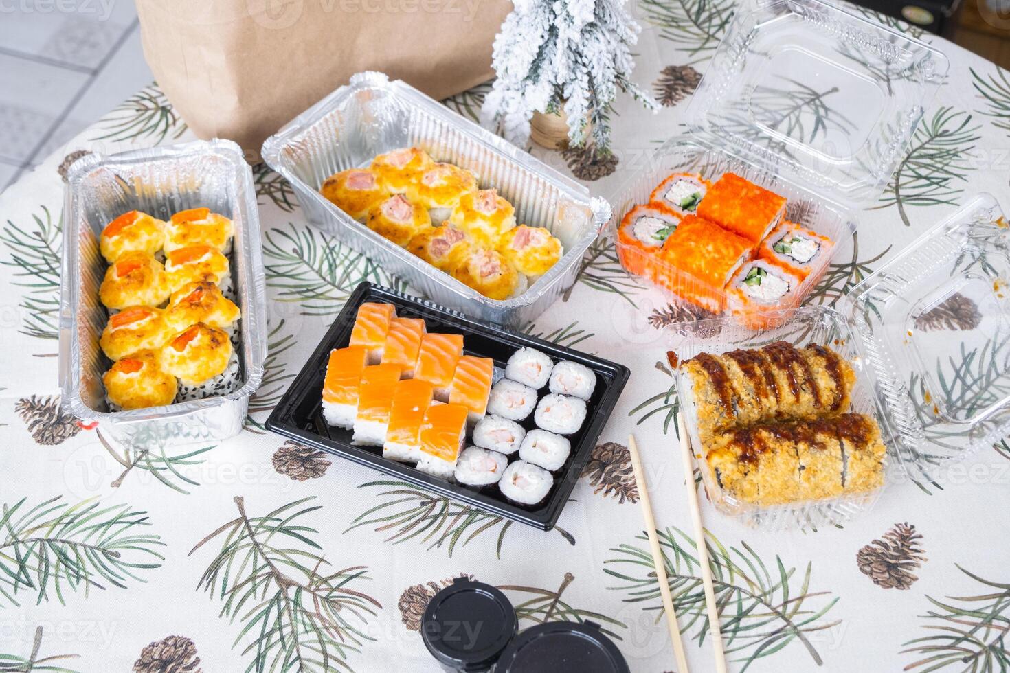 Delivery of sushi and rolls set top view on the table with a Christmas decor with a Christmas tree and a tablecloth with snowflakes, home cooking photo