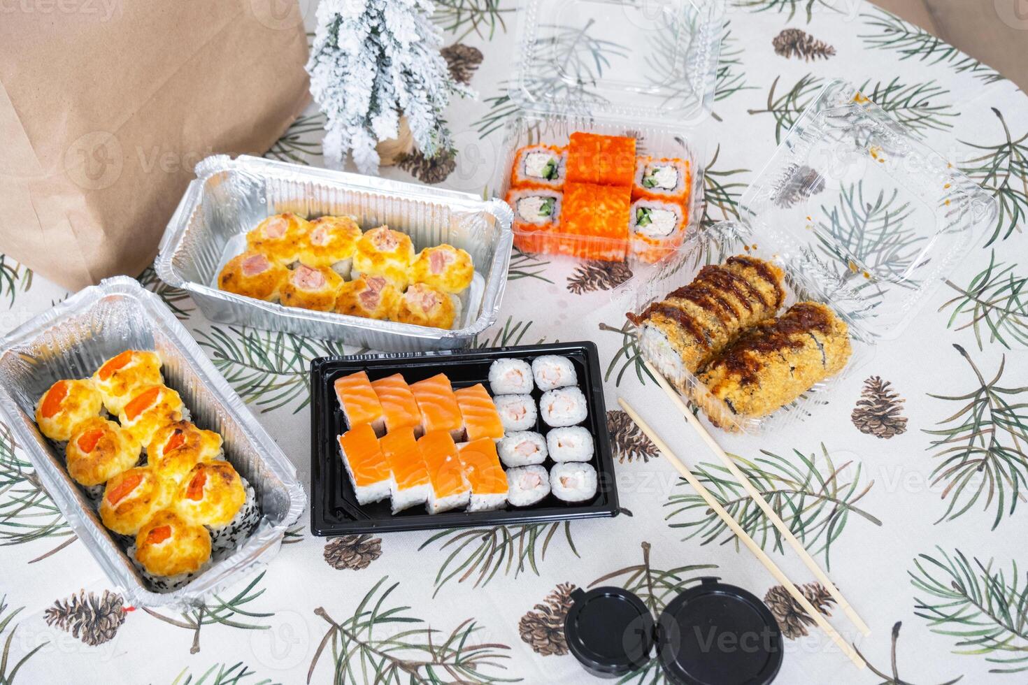 Delivery of sushi and rolls set top view on the table with a Christmas decor with a Christmas tree and a tablecloth with snowflakes, home cooking photo