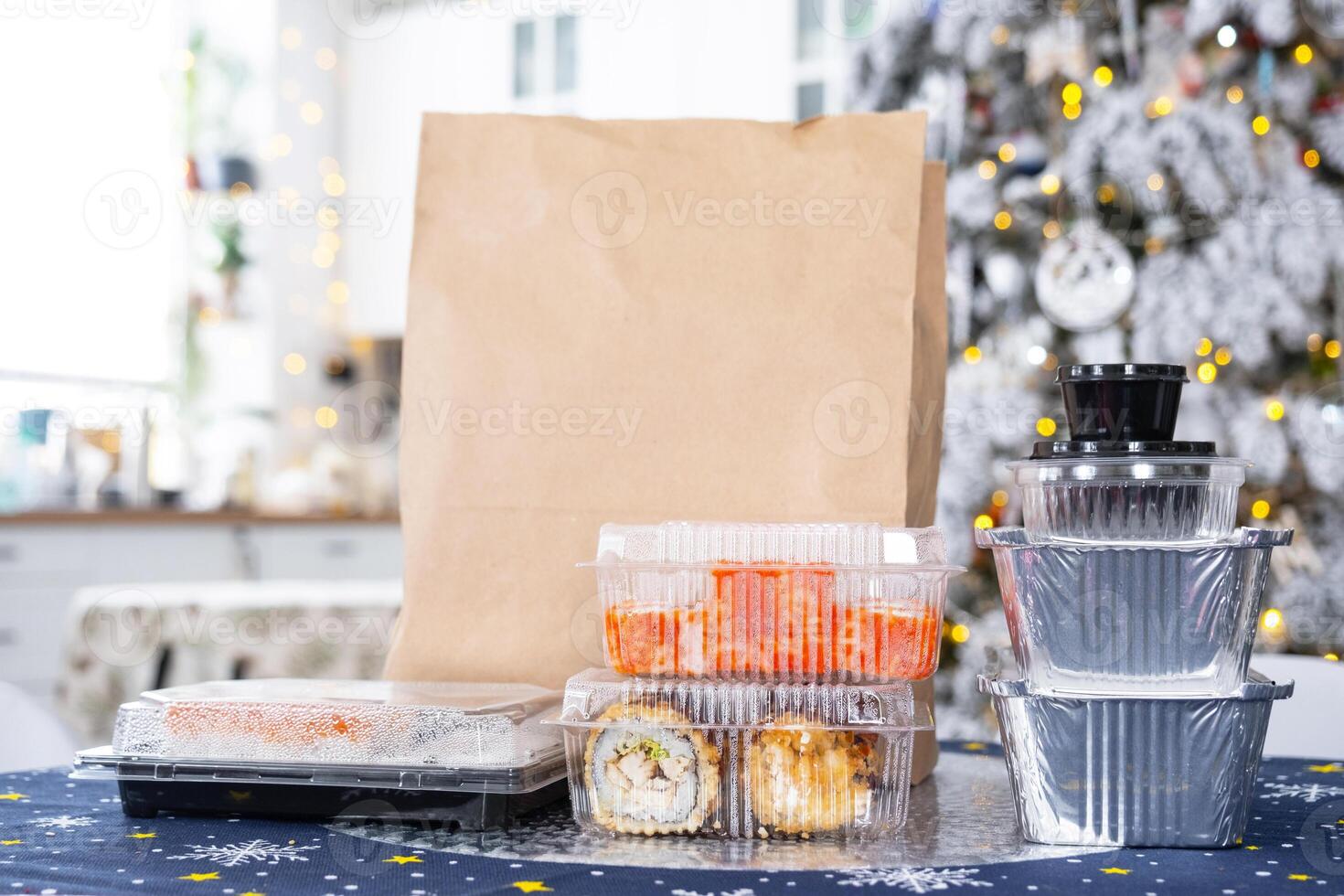 Delivery of sushi and rolls in food containers on the table in the festive interior of the kitchen of the house with a white Christmas tree for Christmas and New year. Food delivery for the holidays photo