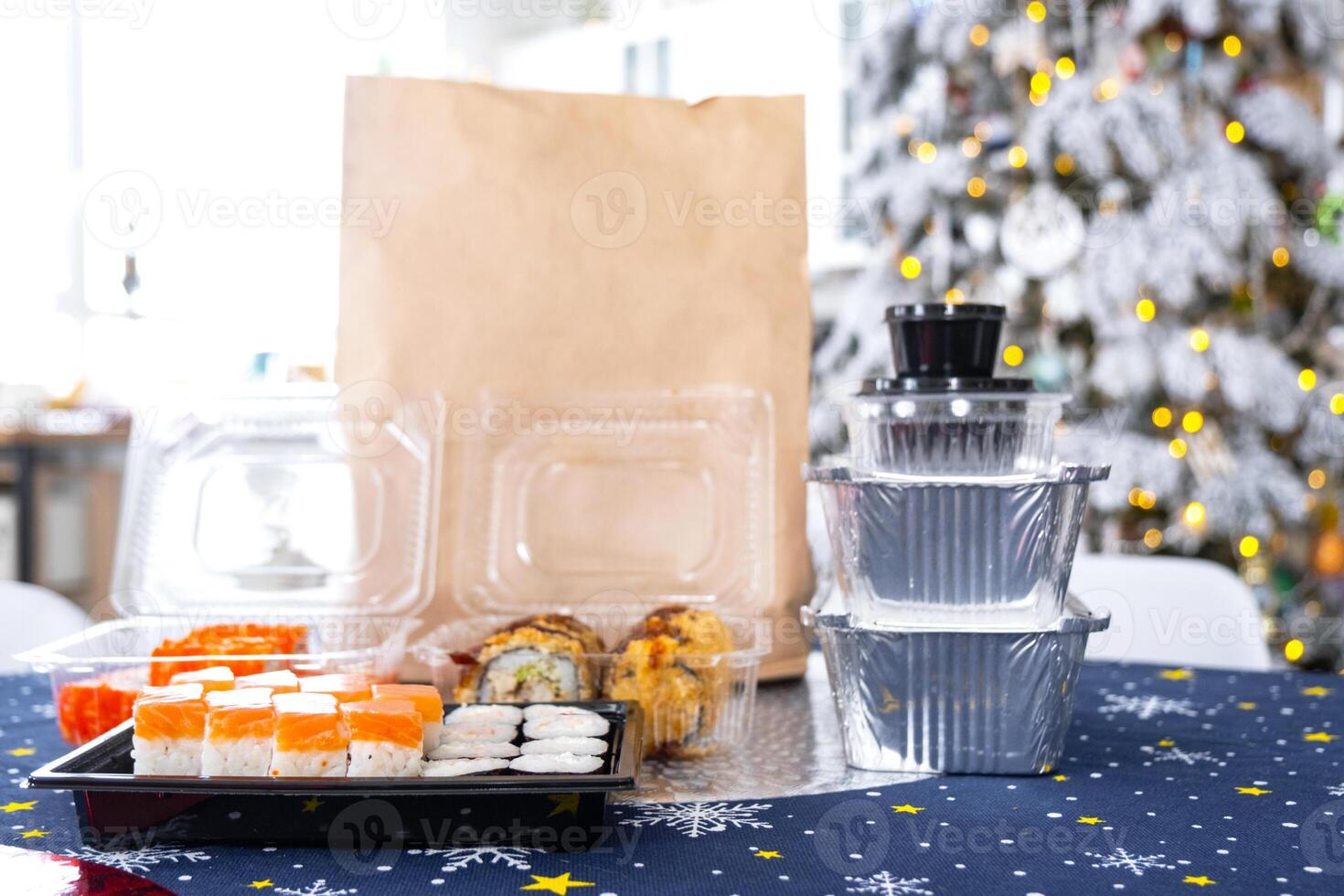 Delivery of sushi and rolls in food containers on the table in the festive interior of the kitchen of the house with a white Christmas tree for Christmas and New year. Food delivery for the holidays photo