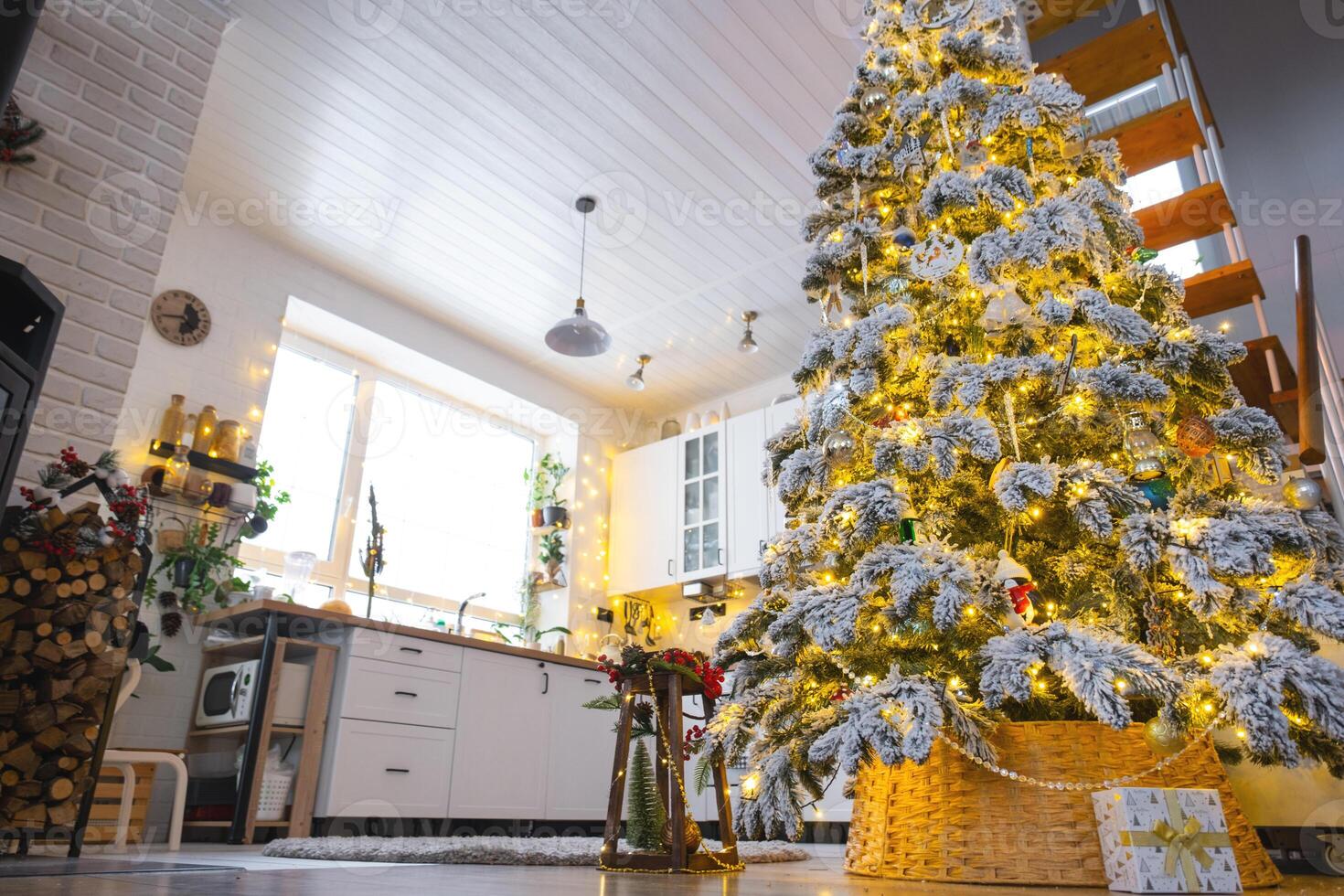Festive Christmas decor in white kitchen, modern village interior with a snowy Christmas tree and fairy lights. New Year, Christmas mood, cozy home, Metal modular staircase. The general plan photo