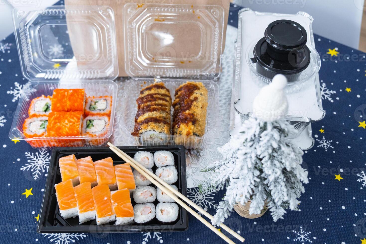 Delivery of sushi and rolls set top view on the table with a Christmas decor with a Christmas tree and a tablecloth with snowflakes, home cooking photo
