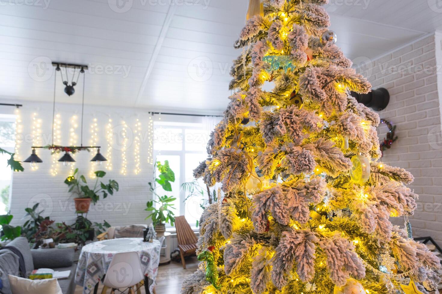 Festive Christmas decor in white kitchen, modern village interior with a snowy Christmas tree and fairy lights. New Year, Christmas mood, cozy home, Metal modular staircase. The general plan photo