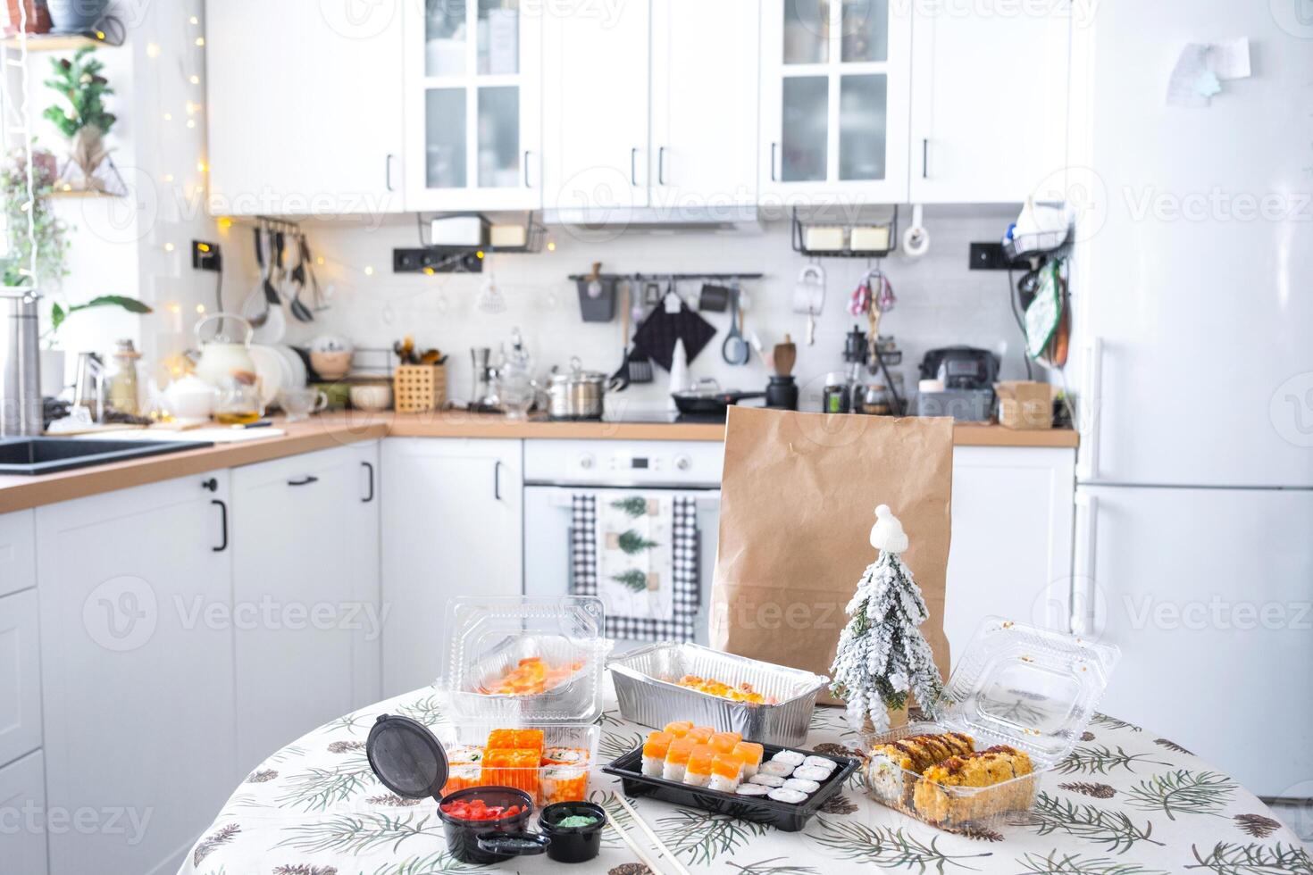 Delivery of sushi and rolls in food containers on the table in the festive interior of the kitchen of the house with a white Christmas tree for Christmas and New year. Food delivery for the holidays photo