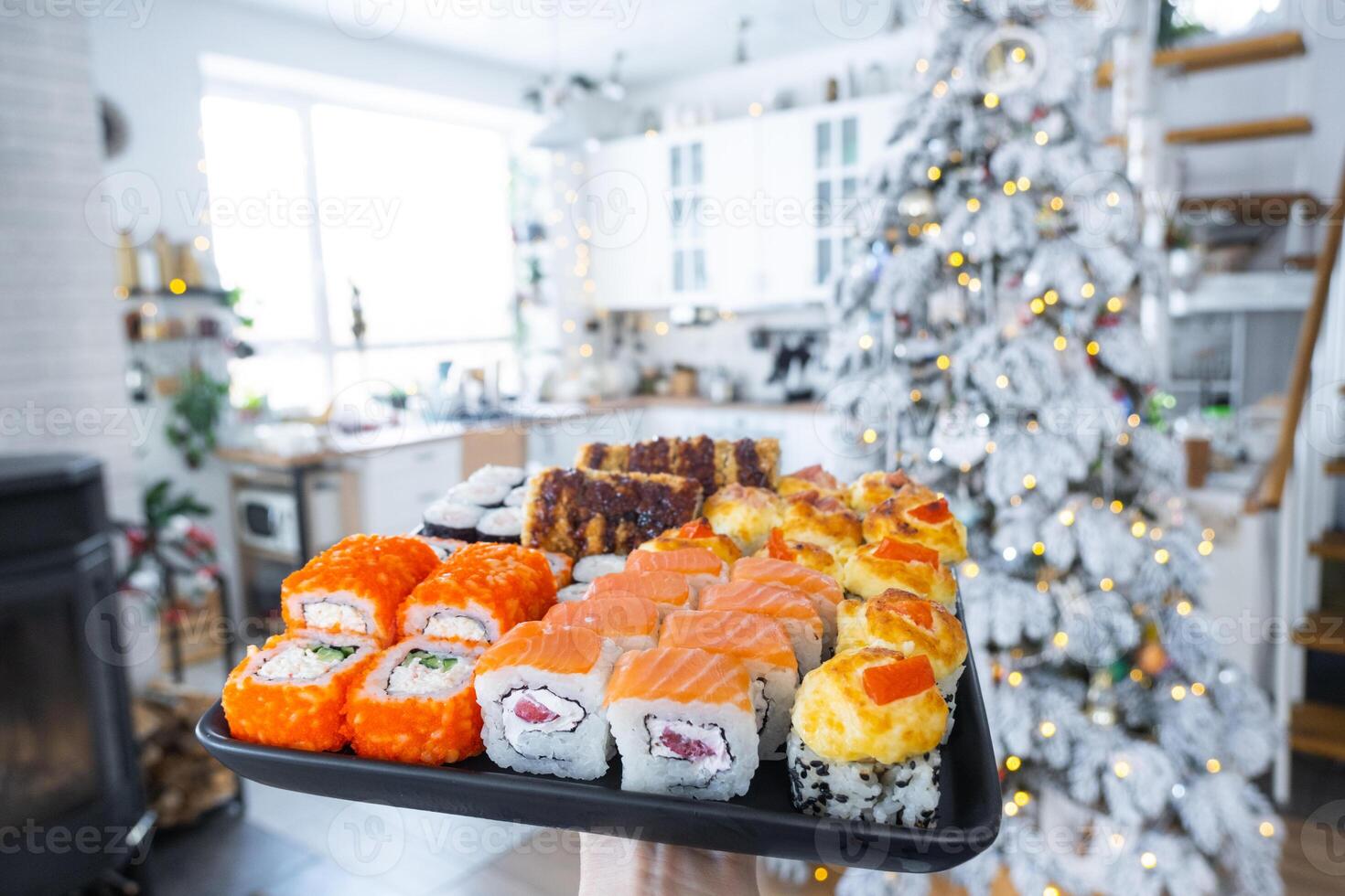 Delivery of sushi and rolls set is hold in hand in the festive interior of house with a white Christmas tree for Christmas and New year. Food delivery for the holidays photo