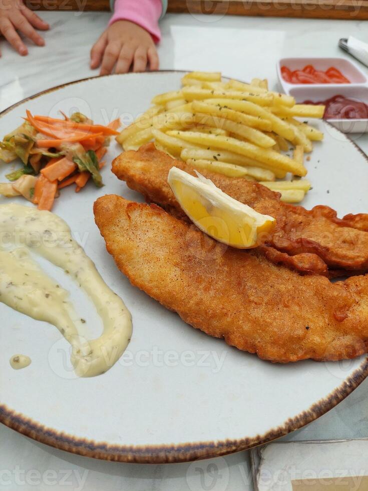 A plate of fish and chips with french fries and a lemon wedge photo