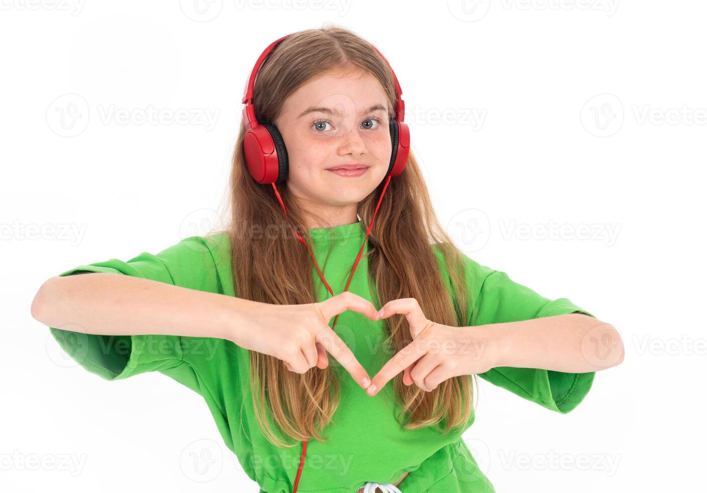 Happy little girl in green summer outfit dancing and gesturing while enjoying music in red headphones on white background photo