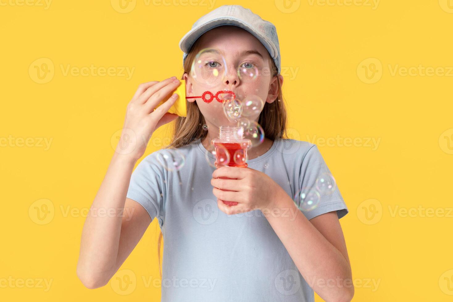 Cute girl blowing soap bubbles on yellow background photo