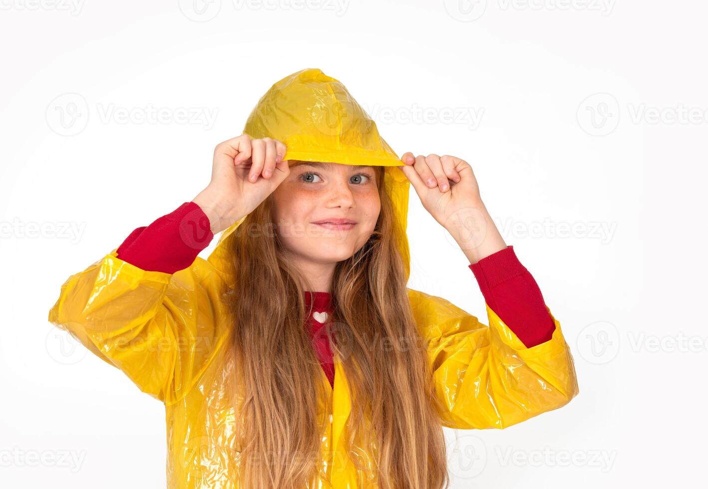 Smiling child girl in yellow raincoat hiding on white background. She is looking up through the transparent hood on rainy sky. Clothes outfit for autumn rainy weather. photo