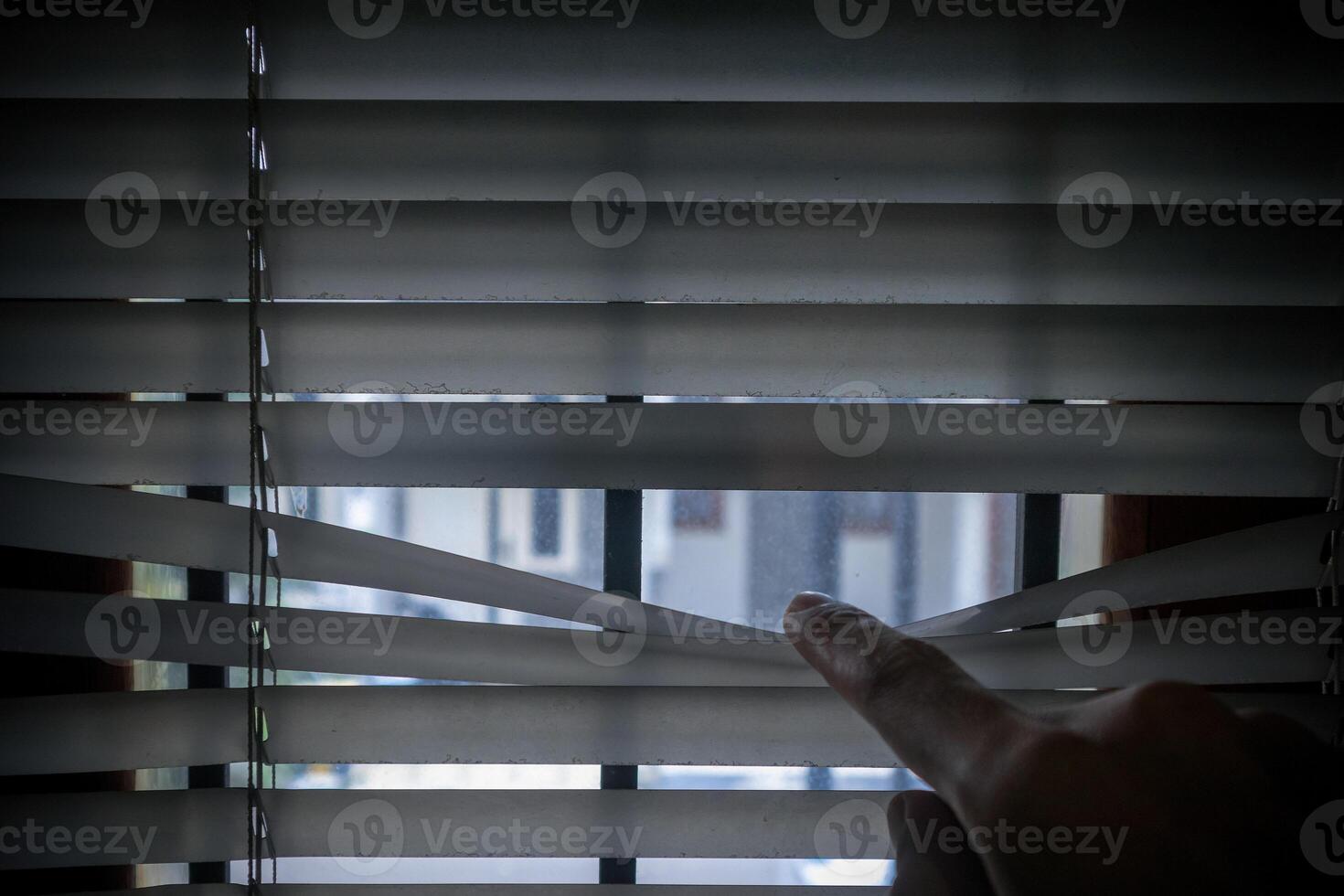 Peeking through window blinds. Hand separating the slats of the window curtain with fingers to look out. photo