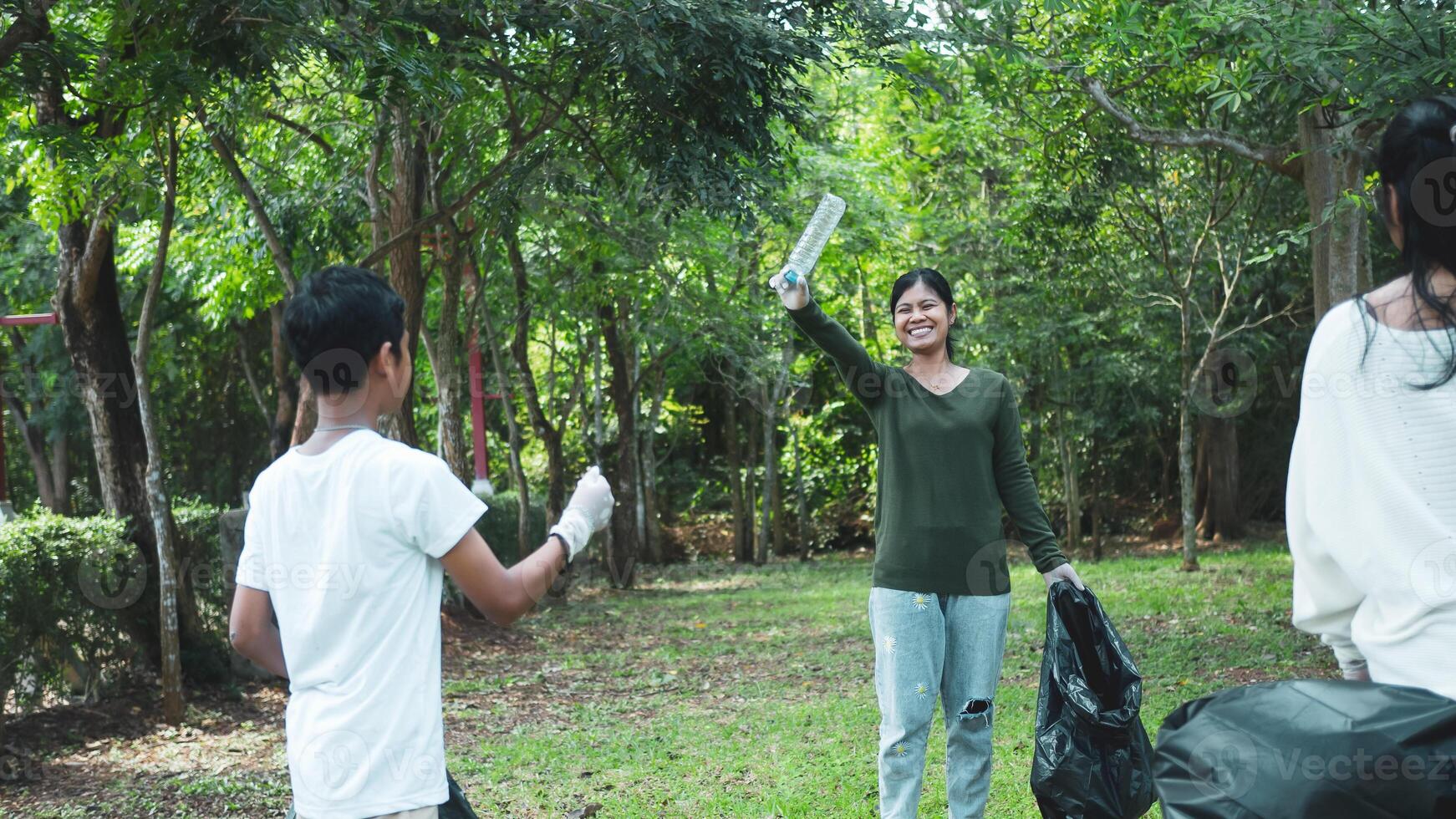 A group of dedicated young volunteers are taking part in an environmental cleaning activity in a park. Volunteers are holding big black bags. People are picking up trash and plastic bottles in a park. photo