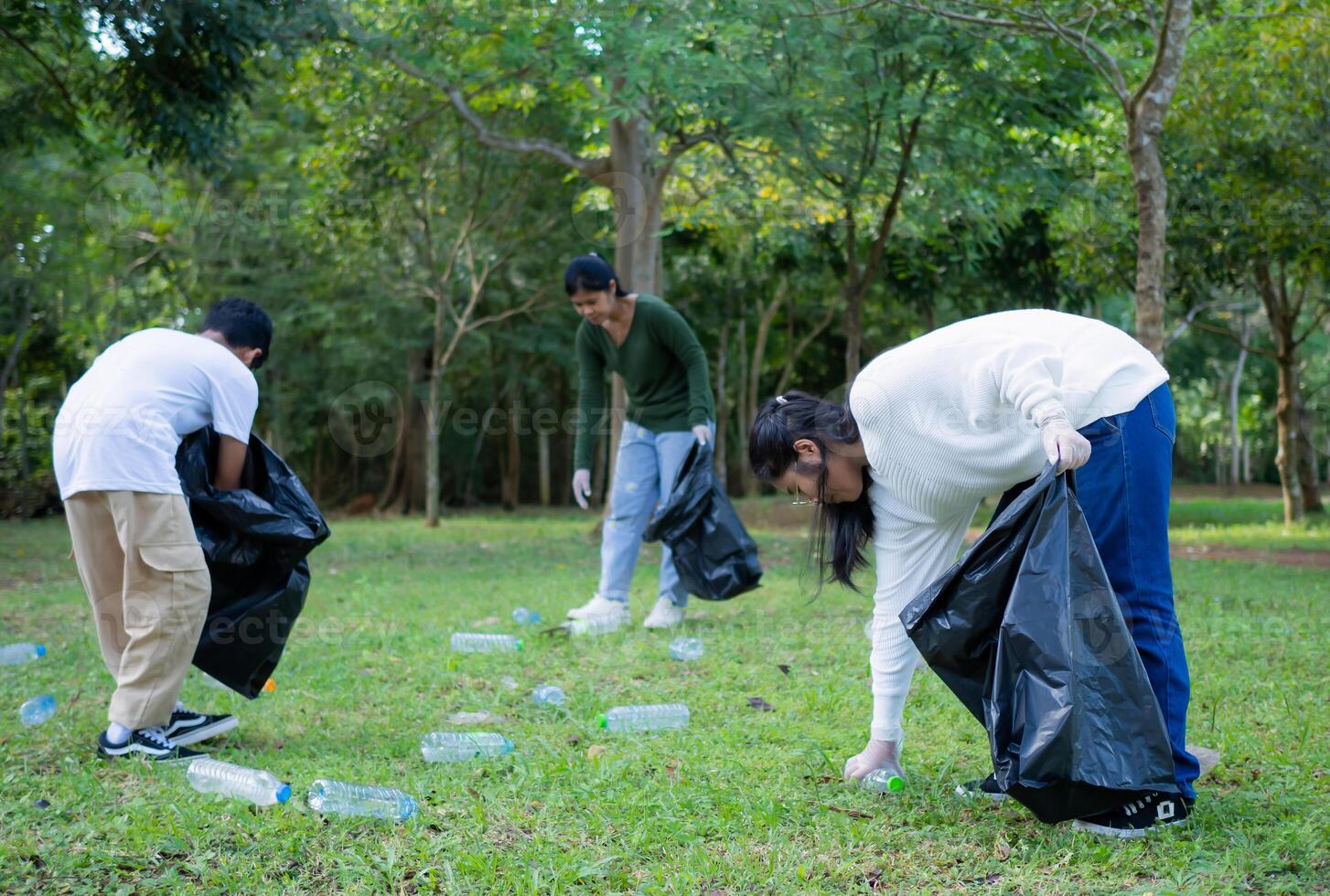 A group of dedicated young volunteers are taking part in an environmental cleaning activity in a park. Volunteers are holding big black bags. People are picking up trash and plastic bottles in a park. photo
