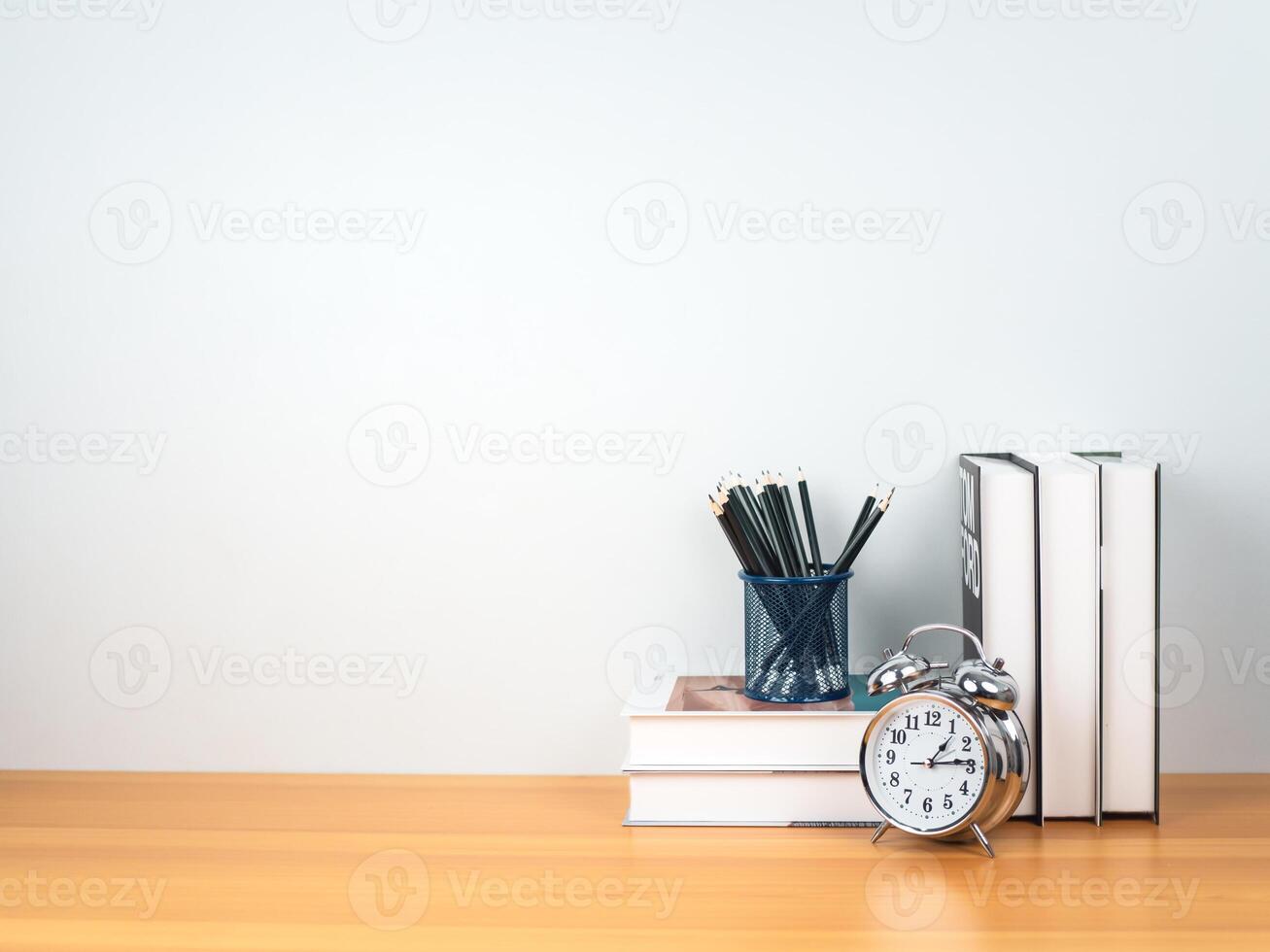 Back to school concept, Pencil on book stack and alarm clock on wooden table workspace area and white wall, Concept of time to study, read books, Concept of preparing for exams. photo