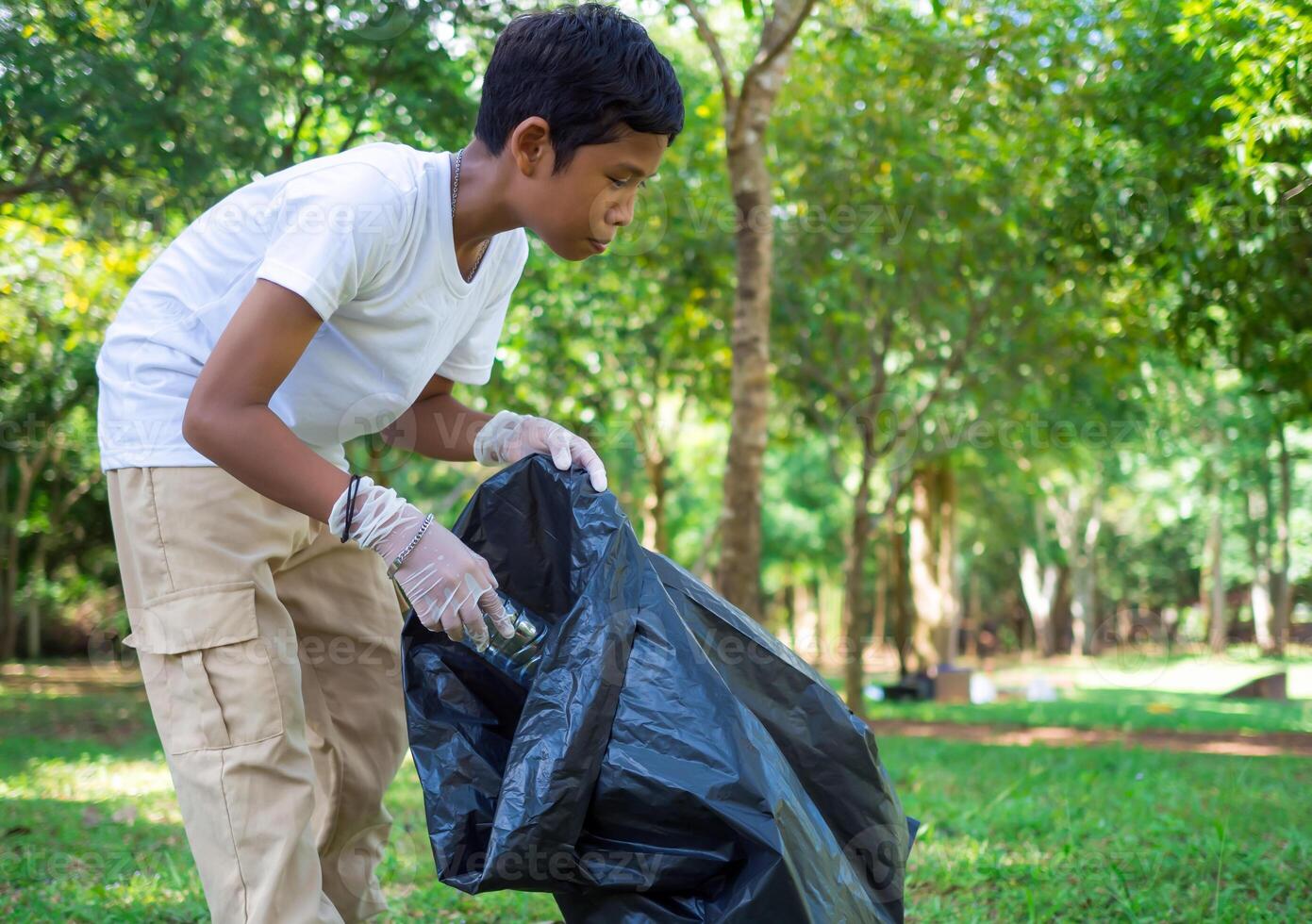 A boy of dedicated volunteers are participating in an environmental cleaning activity in a park. Boy wearing gloves and hold large black bags. Boy collecting trash and plastic bottles in a park. photo