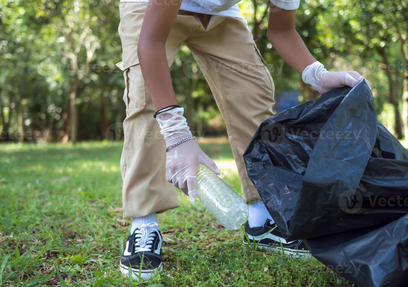 A boy of dedicated volunteers are participating in an environmental cleaning activity in a park. Boy wearing gloves and hold large black bags. Boy collecting trash and plastic bottles in a park. photo