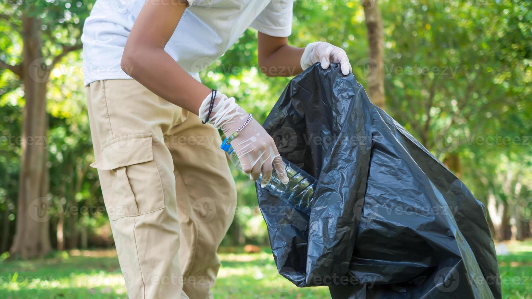 A boy of dedicated volunteers are participating in an environmental cleaning activity in a park. Boy wearing gloves and hold large black bags. Boy collecting trash and plastic bottles in a park. photo