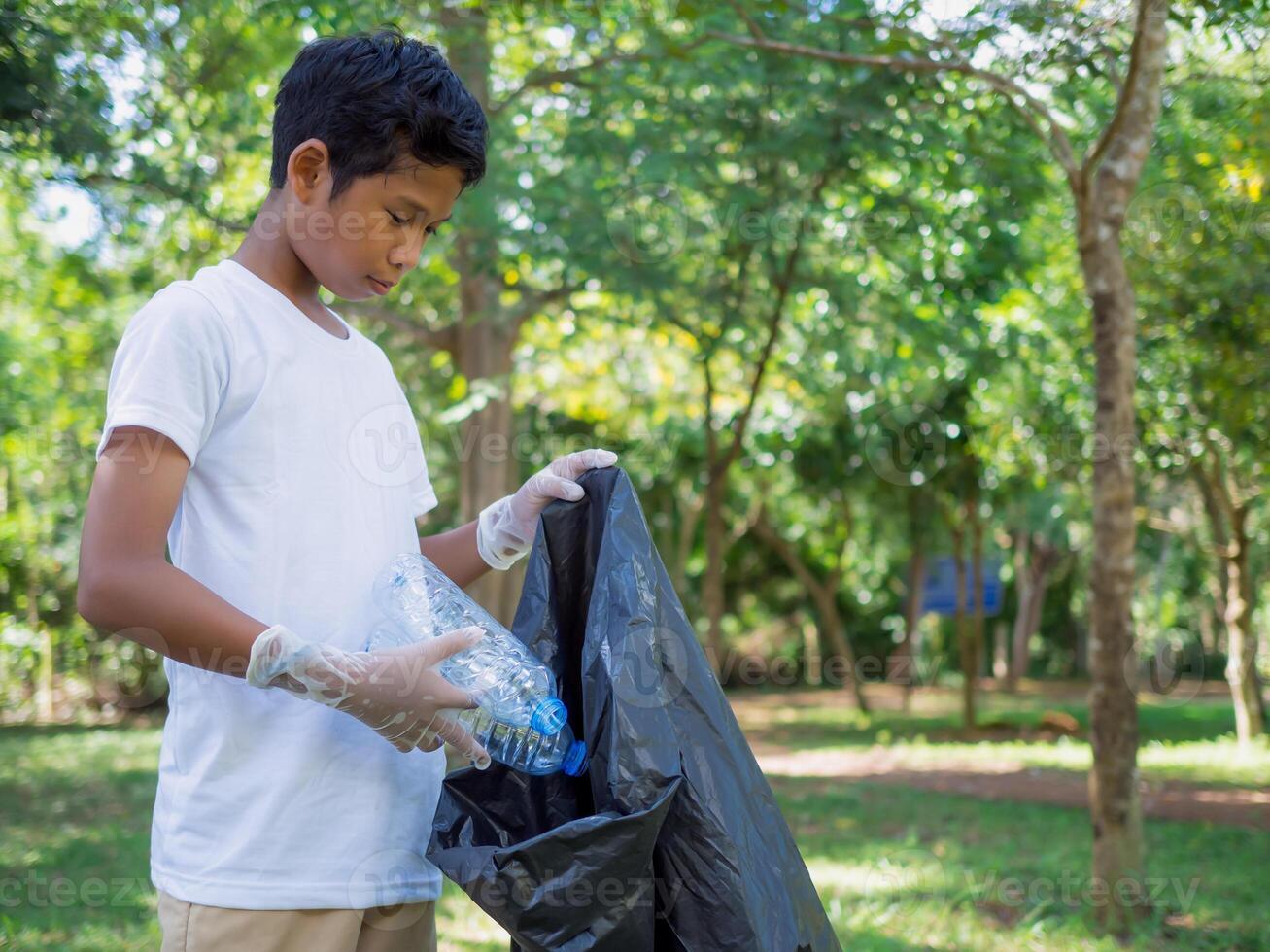 A boy of dedicated volunteers are participating in an environmental cleaning activity in a park. Boy wearing gloves and hold large black bags. Boy collecting trash and plastic bottles in a park. photo