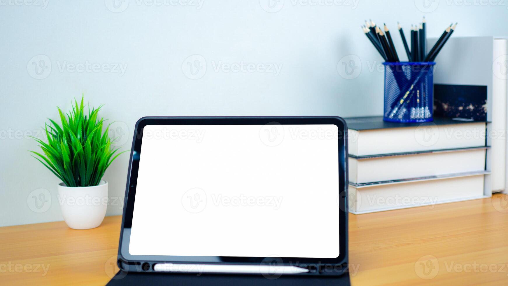 Tablet with blank screen on wooden table. Office supplies, Books, Indoor plants, on wooden table and white wall. Space for copying your text, Workspace and copy space, Desk with office supplies. photo