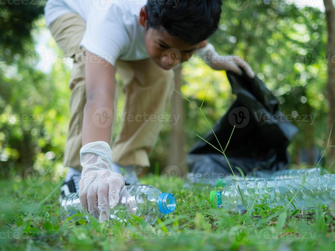 A boy of dedicated volunteers are participating in an environmental cleaning activity in a park. Boy wearing gloves and hold large black bags. Boy collecting trash and plastic bottles in a park. photo