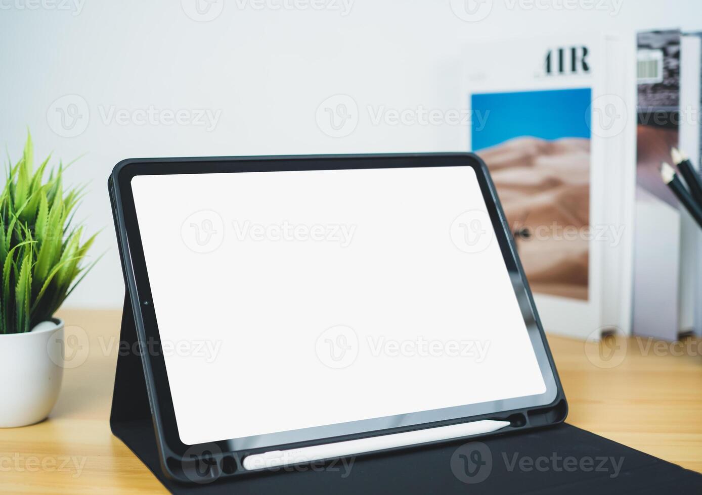 Tablet with blank screen on wooden table. Office supplies, Books, Indoor plants, on wooden table and white wall. Space for copying your text, Workspace and copy space, Desk with office supplies. photo