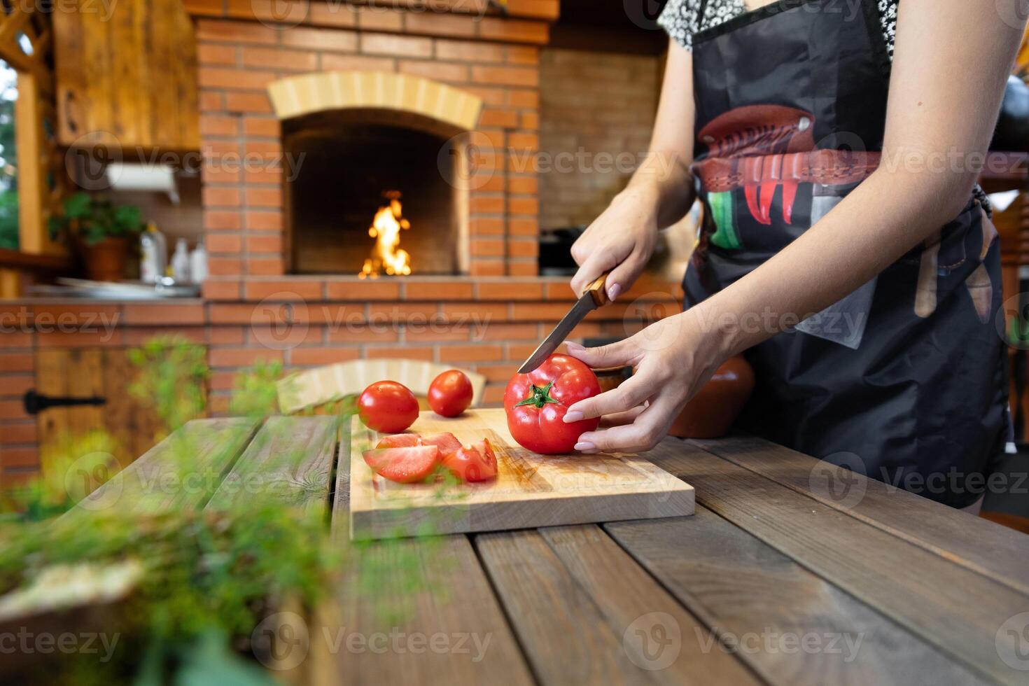 Cutting tomatoes on a wooden cutting board. Cozy kitchen with a brick oven or fireplace in the background, adding warmth. Fresh herbs in the foreground. photo