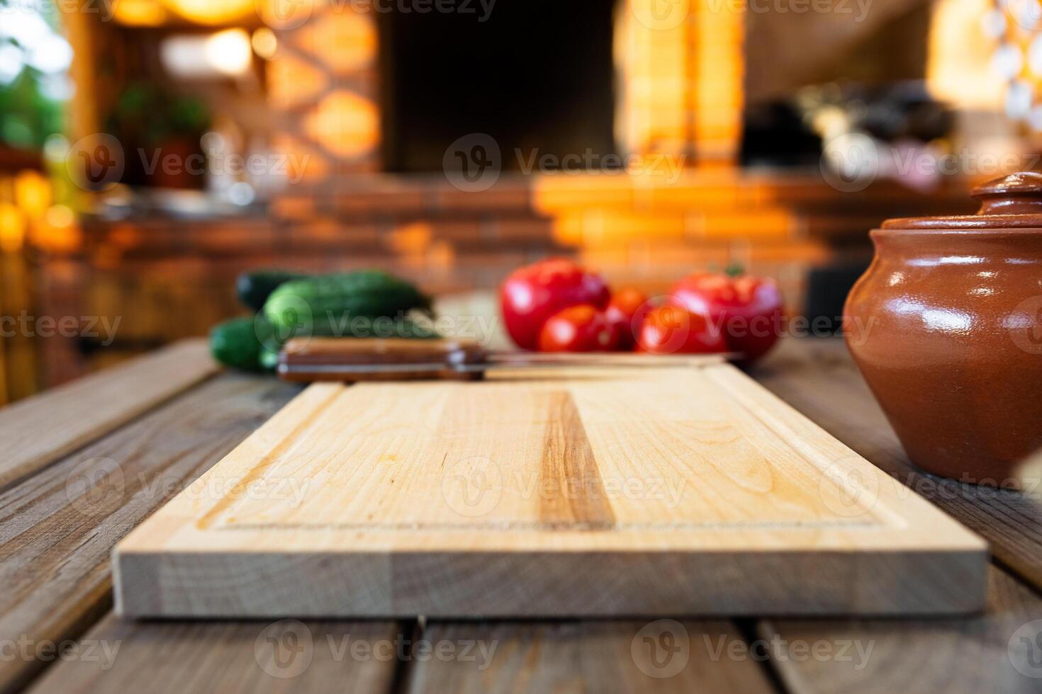Cutting board on a wooden table, surrounded by fresh vegetables like tomatoes and cucumbers. Rustic kitchen with natural lighting and a brick backdrop. photo