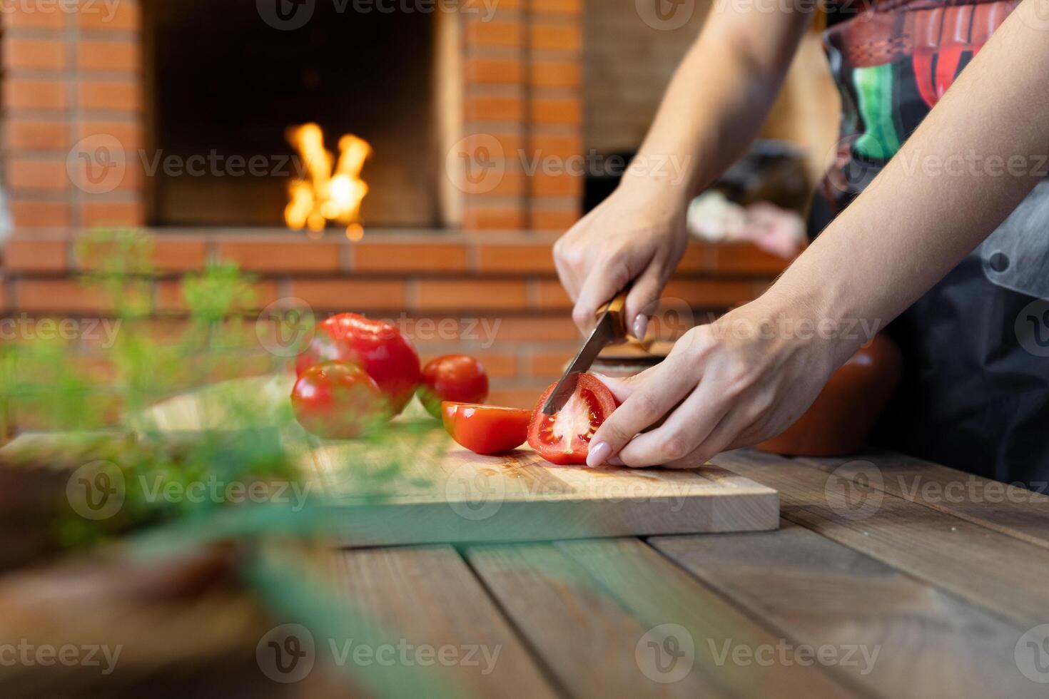 Cutting tomatoes on a wooden cutting board. Cozy kitchen with a brick oven or fireplace in the background, adding warmth. Fresh herbs in the foreground. photo