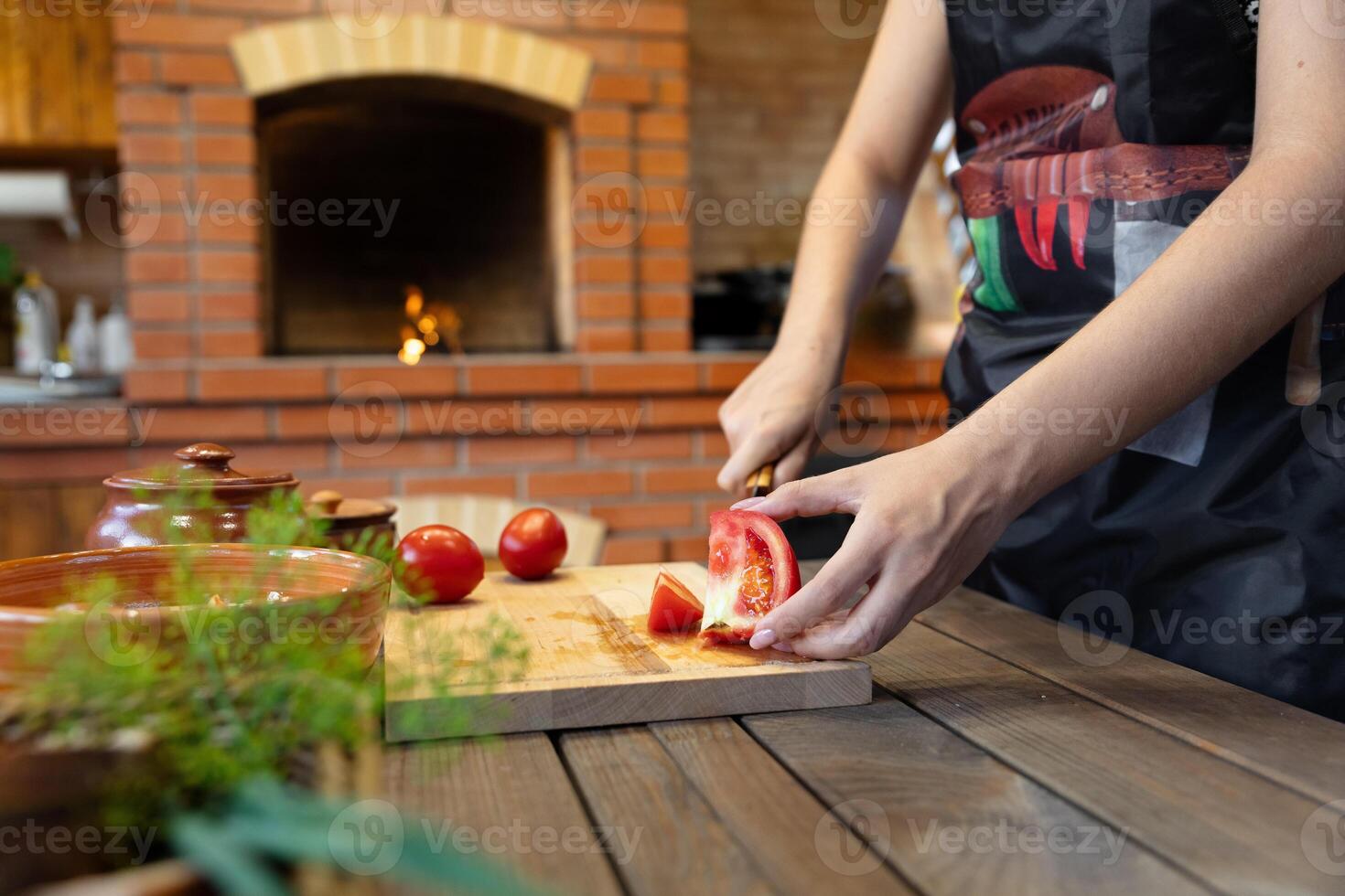 Cutting tomatoes on a wooden cutting board. Cozy kitchen with a brick oven or fireplace in the background, adding warmth. Fresh herbs in the foreground. photo