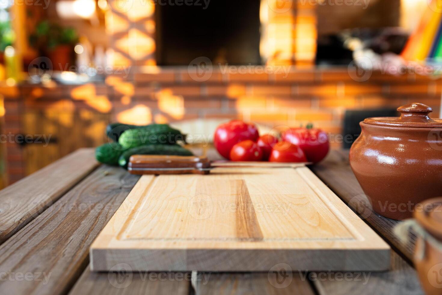 Cutting board on a wooden table, surrounded by fresh vegetables like tomatoes and cucumbers. Rustic kitchen with natural lighting and a brick backdrop. photo