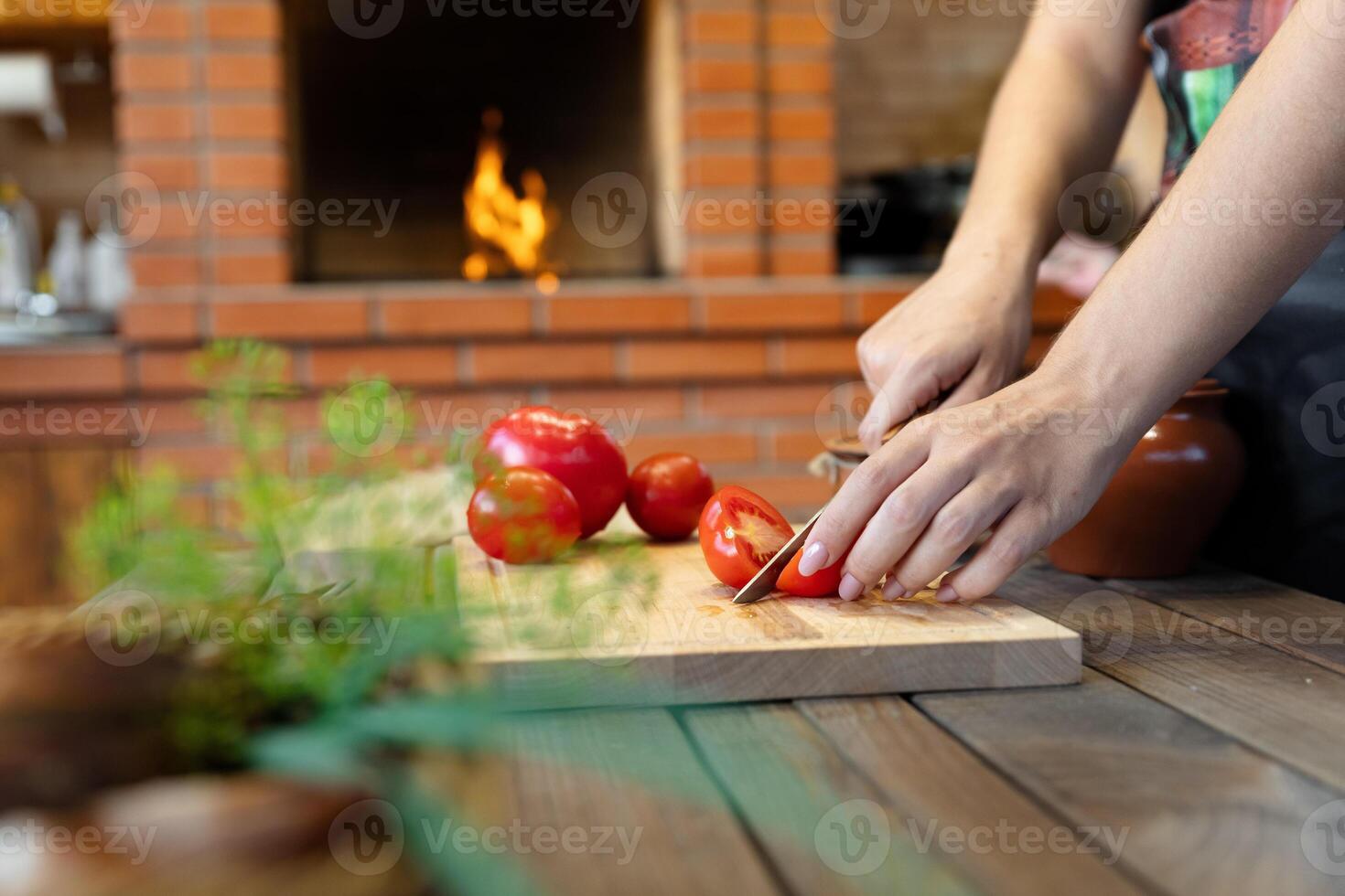 Cutting tomatoes on a wooden cutting board. Cozy kitchen with a brick oven or fireplace in the background, adding warmth. Fresh herbs in the foreground. photo