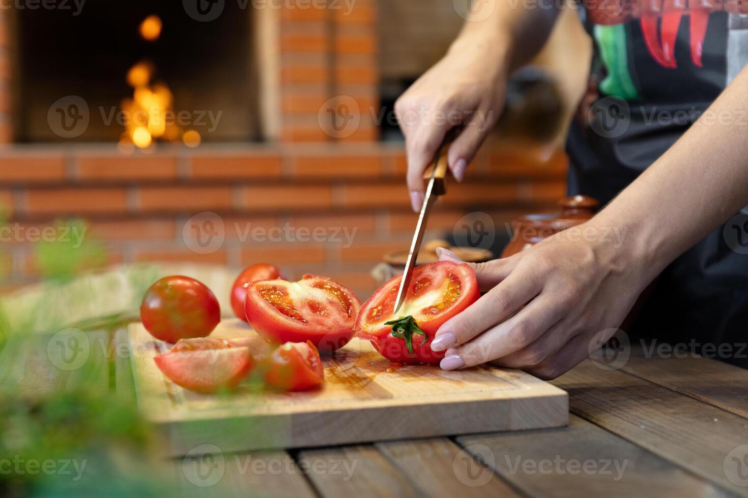 Cutting tomatoes on a wooden cutting board. Cozy kitchen with a brick oven or fireplace in the background, adding warmth. Fresh herbs in the foreground. photo