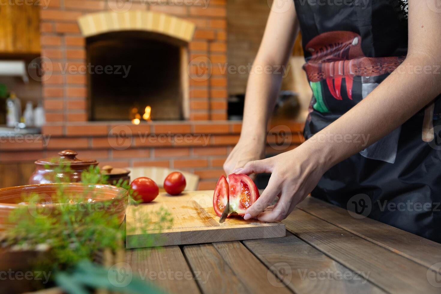 Cutting tomatoes on a wooden cutting board. Cozy kitchen with a brick oven or fireplace in the background, adding warmth. Fresh herbs in the foreground. photo