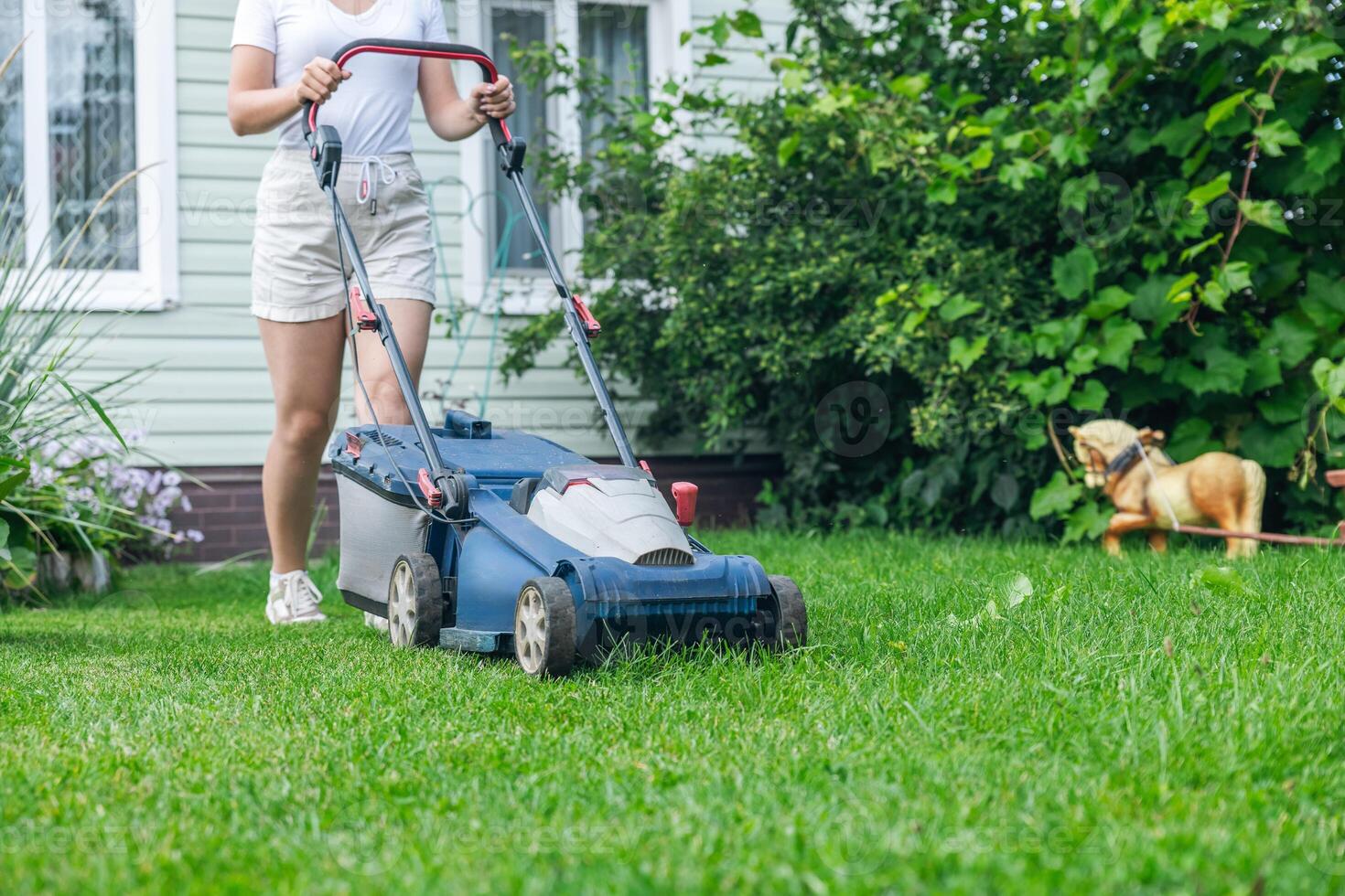 A lawn mower is cutting green grass, the gardener with a lawn mower is working in the backyard, a side view. photo