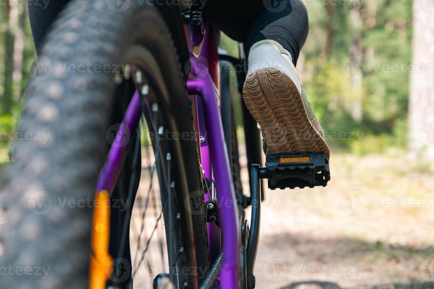 Close-up of a bicycle parked on a dirt trail, with a focus on the kickstand. The bike's rugged tires are well-suited for trail riding, and the scene suggests a forest environment. photo
