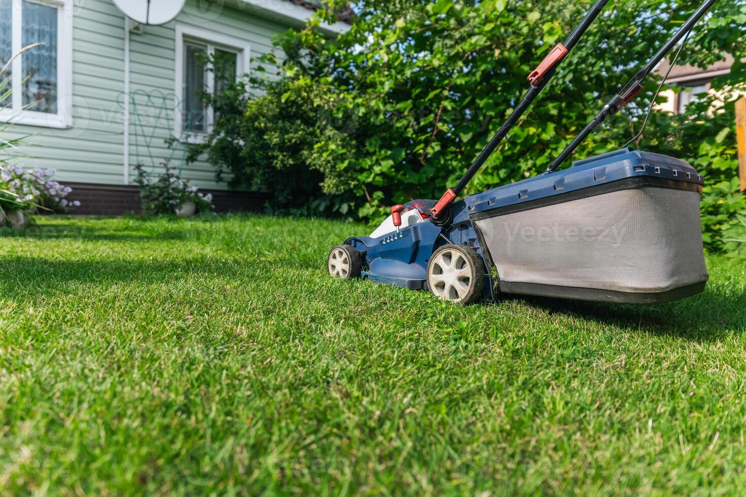 A lawn mower is cutting green grass, the gardener with a lawn mower is working in the backyard, a side view. photo