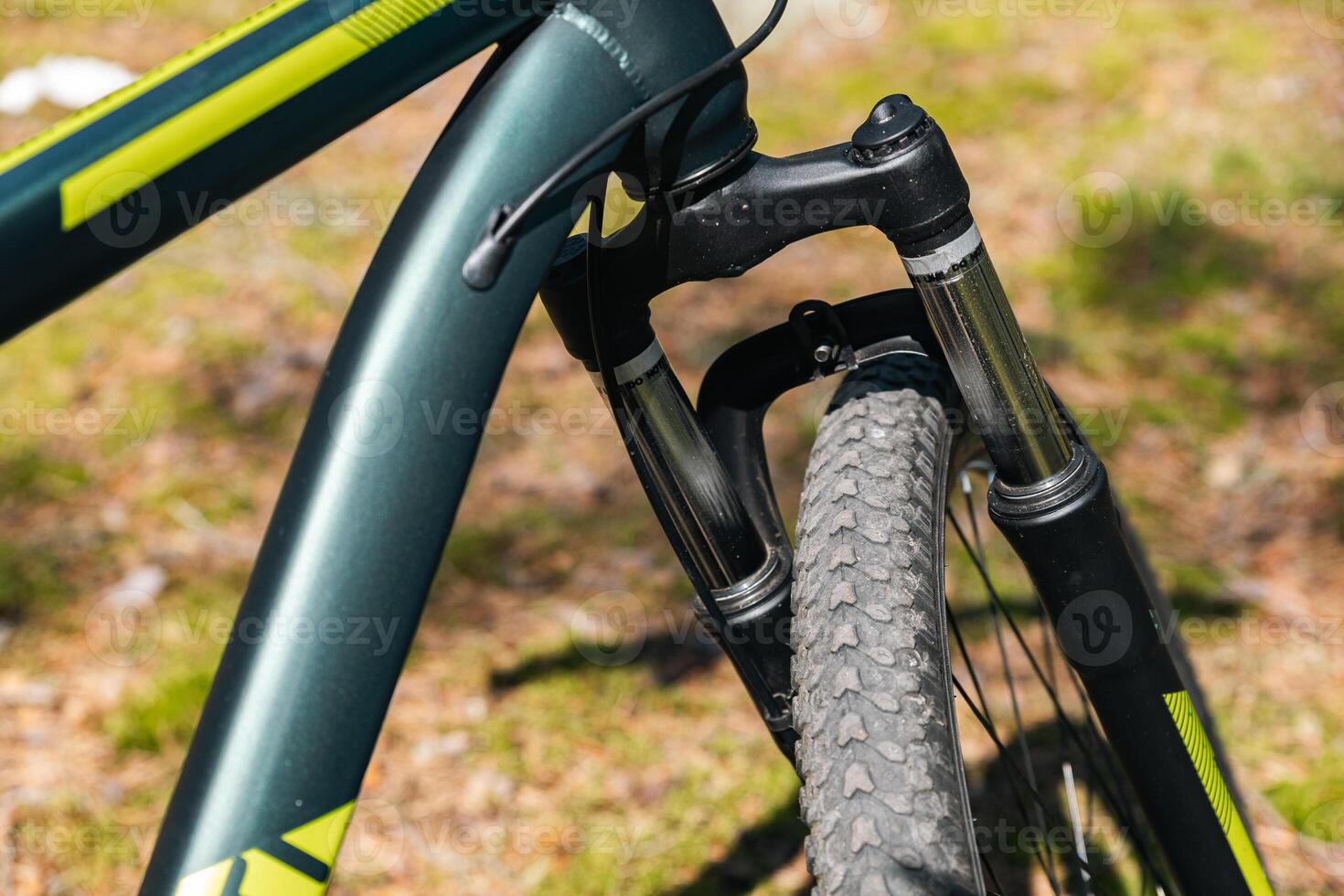 Close-up of a bicycle parked on a dirt trail, with a focus on the kickstand. The bike's rugged tires are well-suited for trail riding, and the scene suggests a forest environment. photo