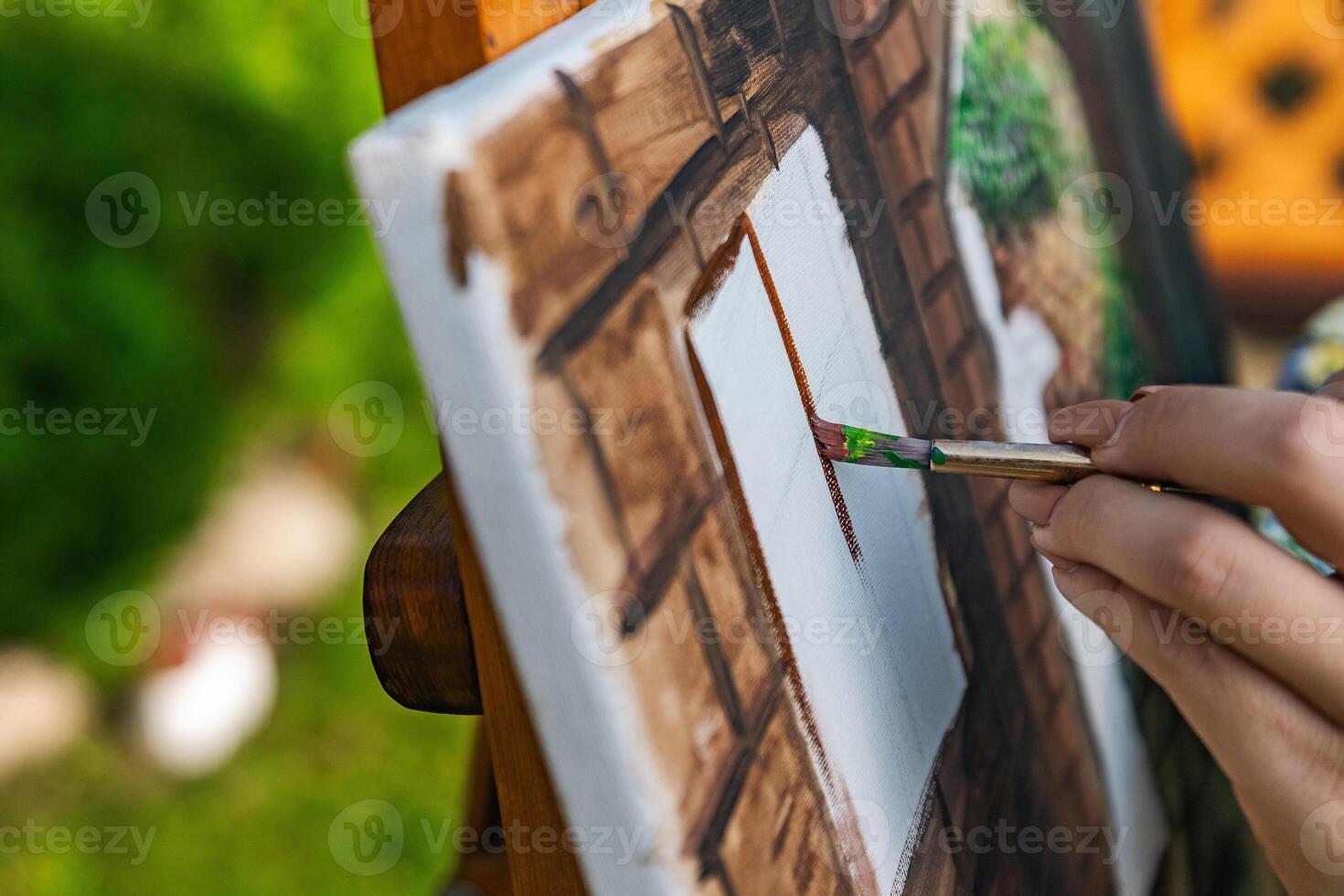 Close-up of someone skillfully painting on a canvas. The artwork looks like it depicts a rustic scene, possibly featuring elements like bricks or wood, giving it a cozy, homely feel. photo