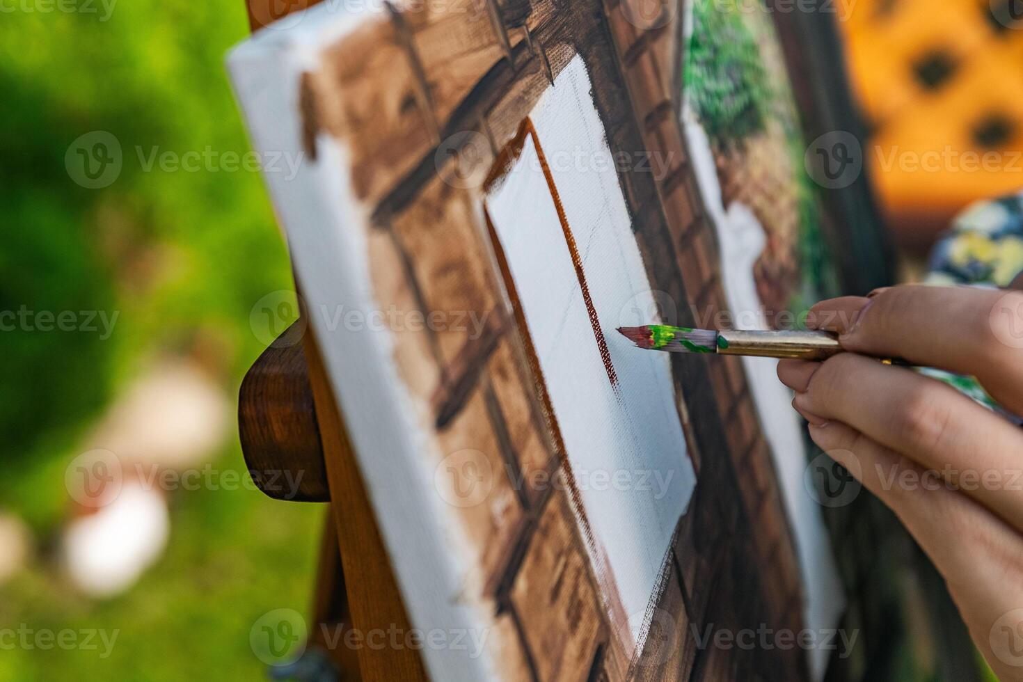 Close-up of someone skillfully painting on a canvas. The artwork looks like it depicts a rustic scene, possibly featuring elements like bricks or wood, giving it a cozy, homely feel. photo