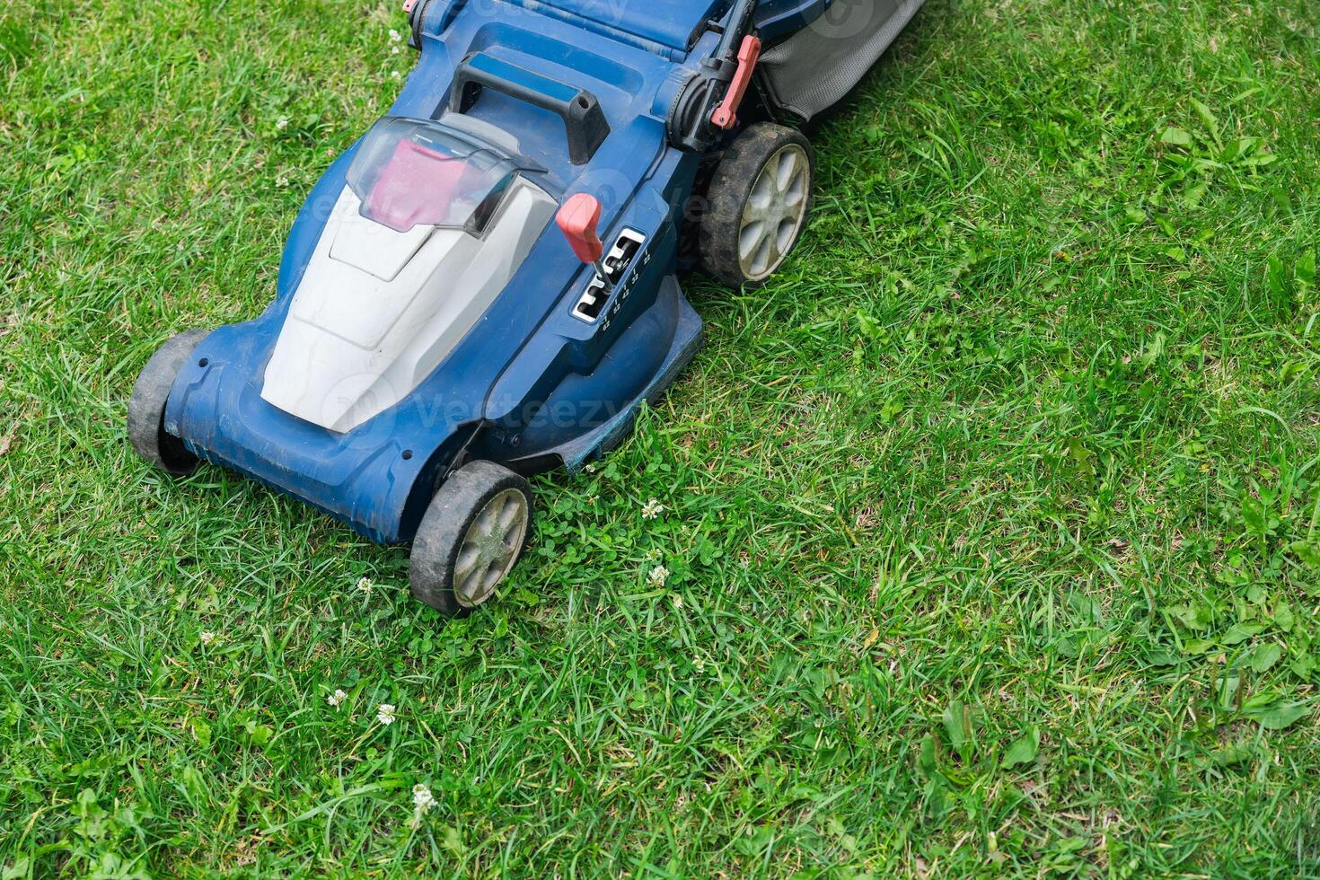 Lawn mower cutting green grass in backyard. Gardening background. photo