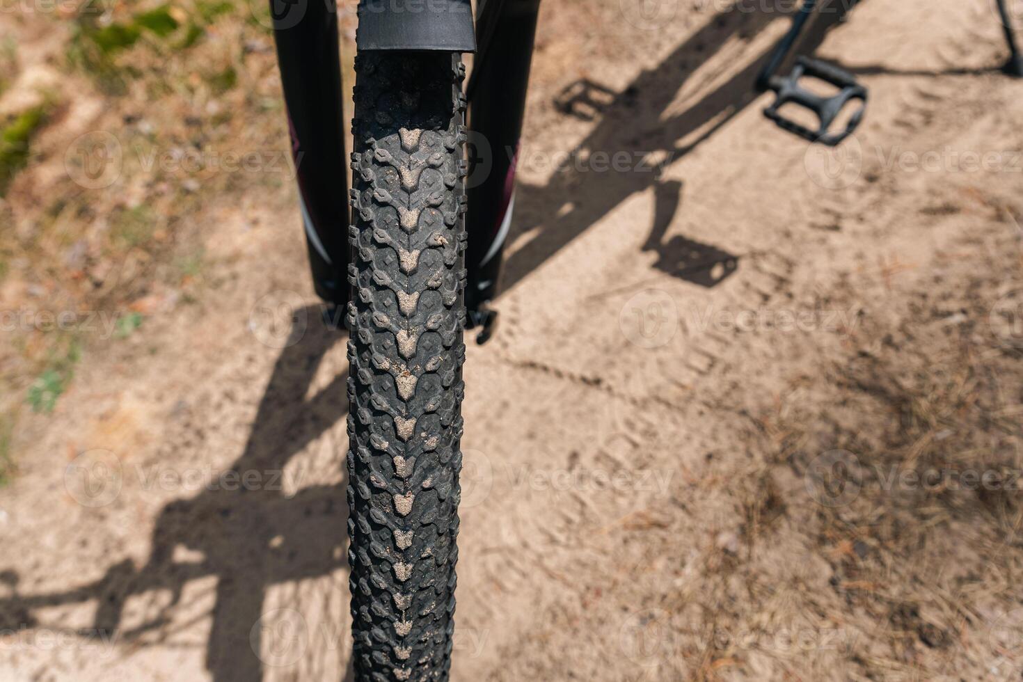 Close-up of a bicycle parked on a dirt trail, with a focus on the kickstand. The bike's rugged tires are well-suited for trail riding, and the scene suggests a forest environment. photo