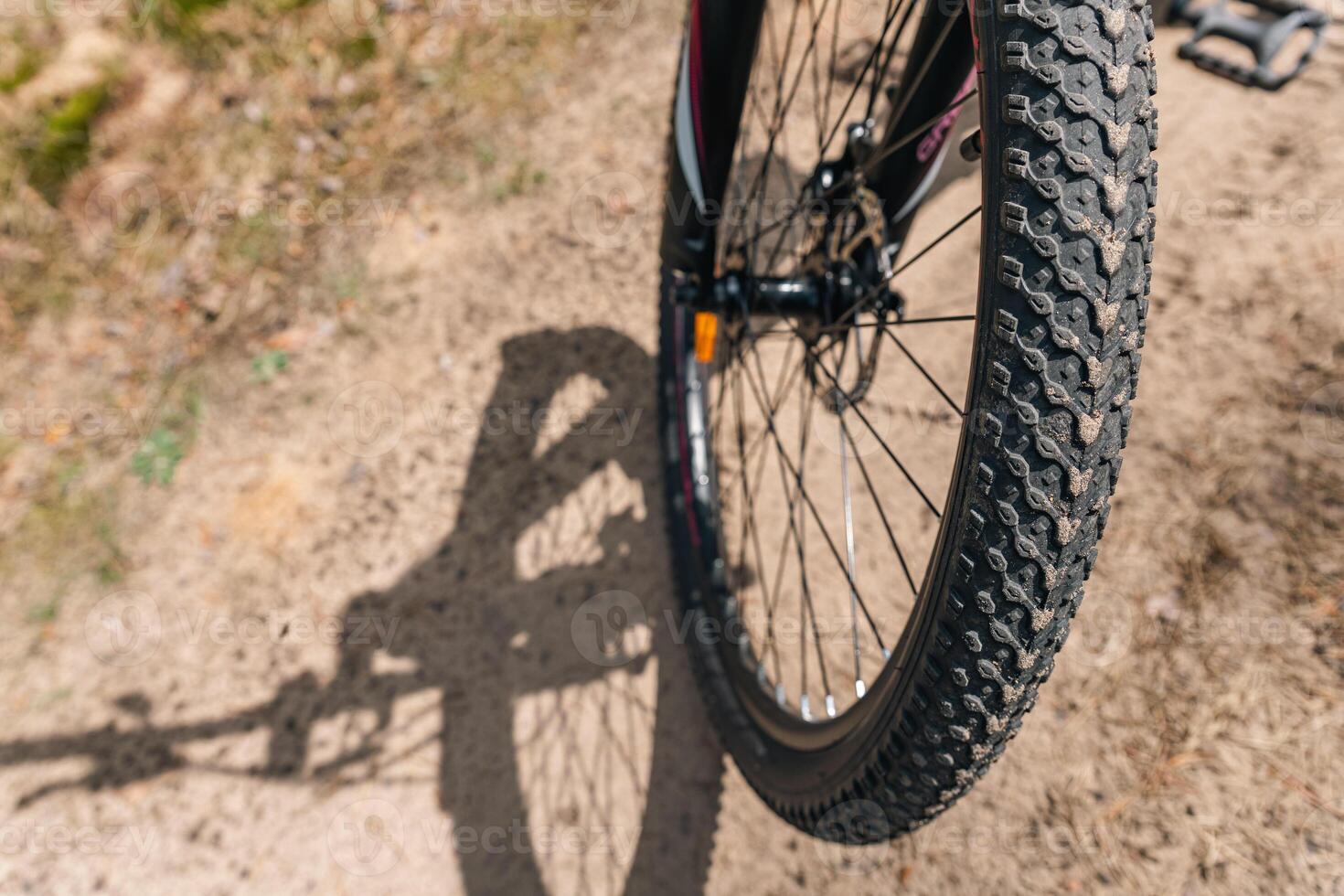 Close-up of a bicycle parked on a dirt trail, with a focus on the kickstand. The bike's rugged tires are well-suited for trail riding, and the scene suggests a forest environment. photo