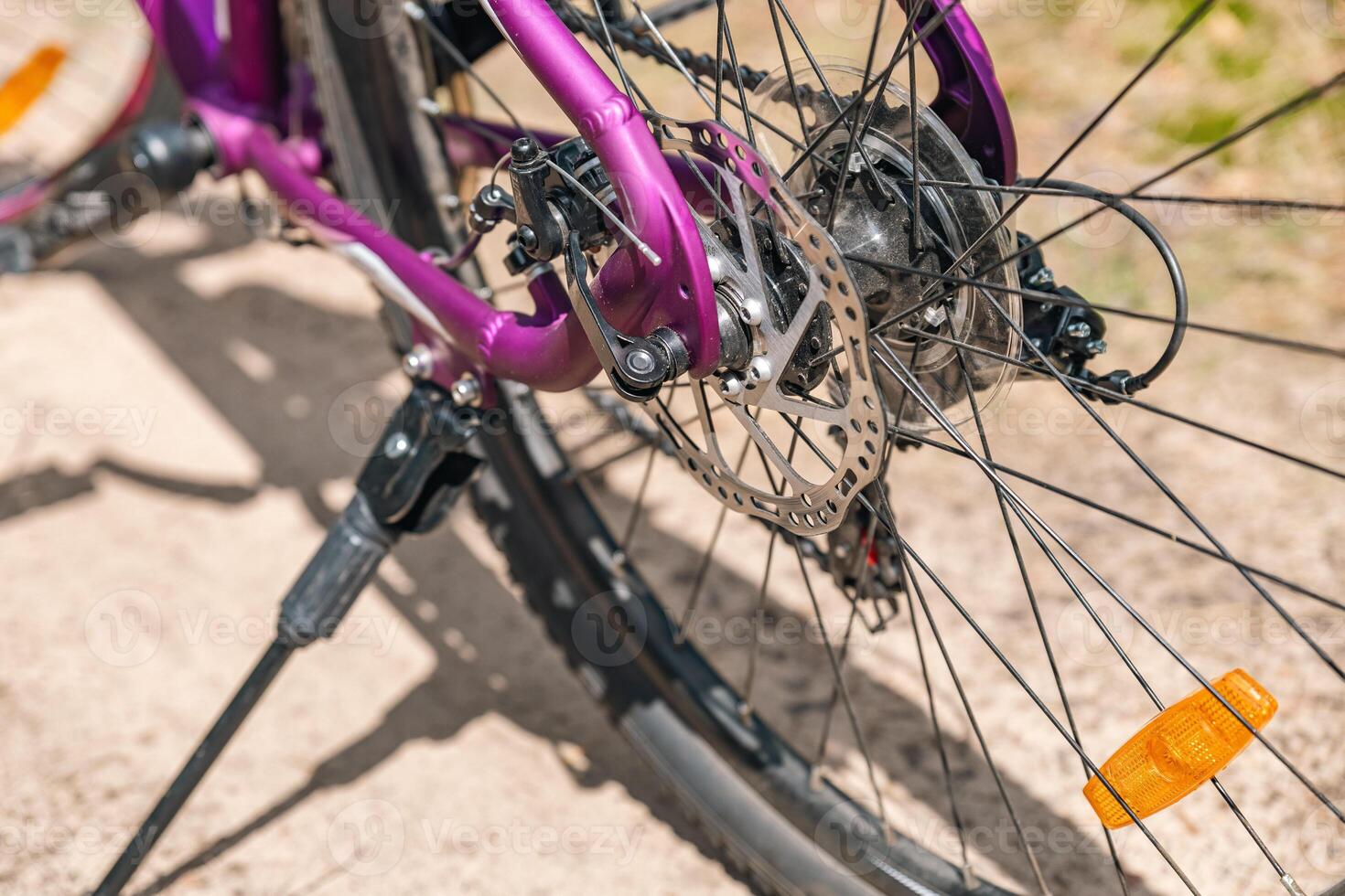 Close-up of a bicycle parked on a dirt trail, with a focus on the kickstand. The bike's rugged tires are well-suited for trail riding, and the scene suggests a forest environment. photo