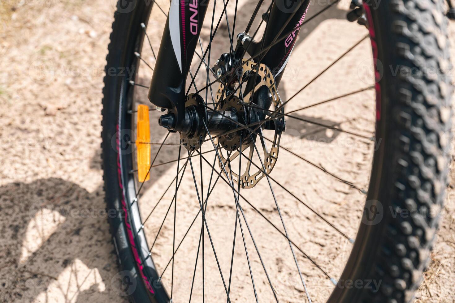Close-up of a bicycle parked on a dirt trail, with a focus on the kickstand. The bike's rugged tires are well-suited for trail riding, and the scene suggests a forest environment. photo