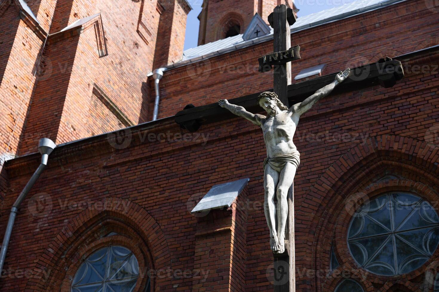 Exterior of a Gothic-style church, with its red brick facade and tall, pointed spires that reach into the sky. Prominently featured is a crucifix, symbolizing the crucifixion of Jesus Christ. photo