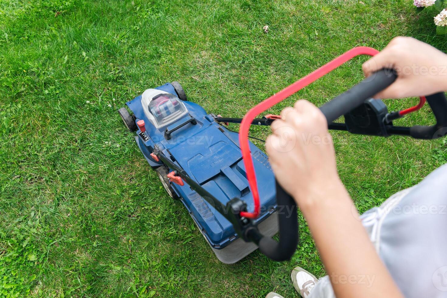 This image captures someone mowing their lawn with a push lawn mower. The person is holding onto the handle, guiding the mower over a well-maintained grassy area. photo