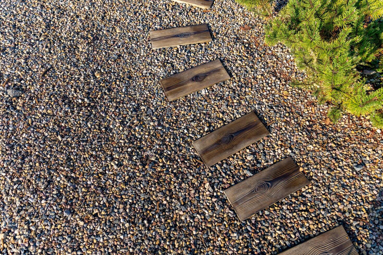 Pathway made of wooden planks placed on a bed of gravel. The wooden planks are arranged in a winding pattern, creating a natural and inviting walkway. The gravel surrounding the planks. photo