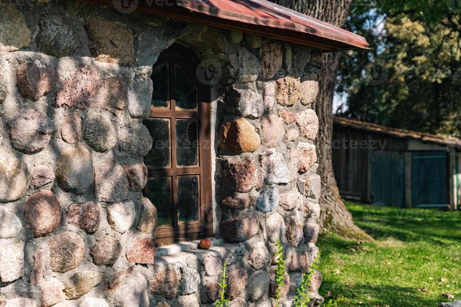 Rustic stone building with a charming window. The wall is built from irregularly shaped stones, adding to its natural and historical charm. The window, framed in dark wood. photo
